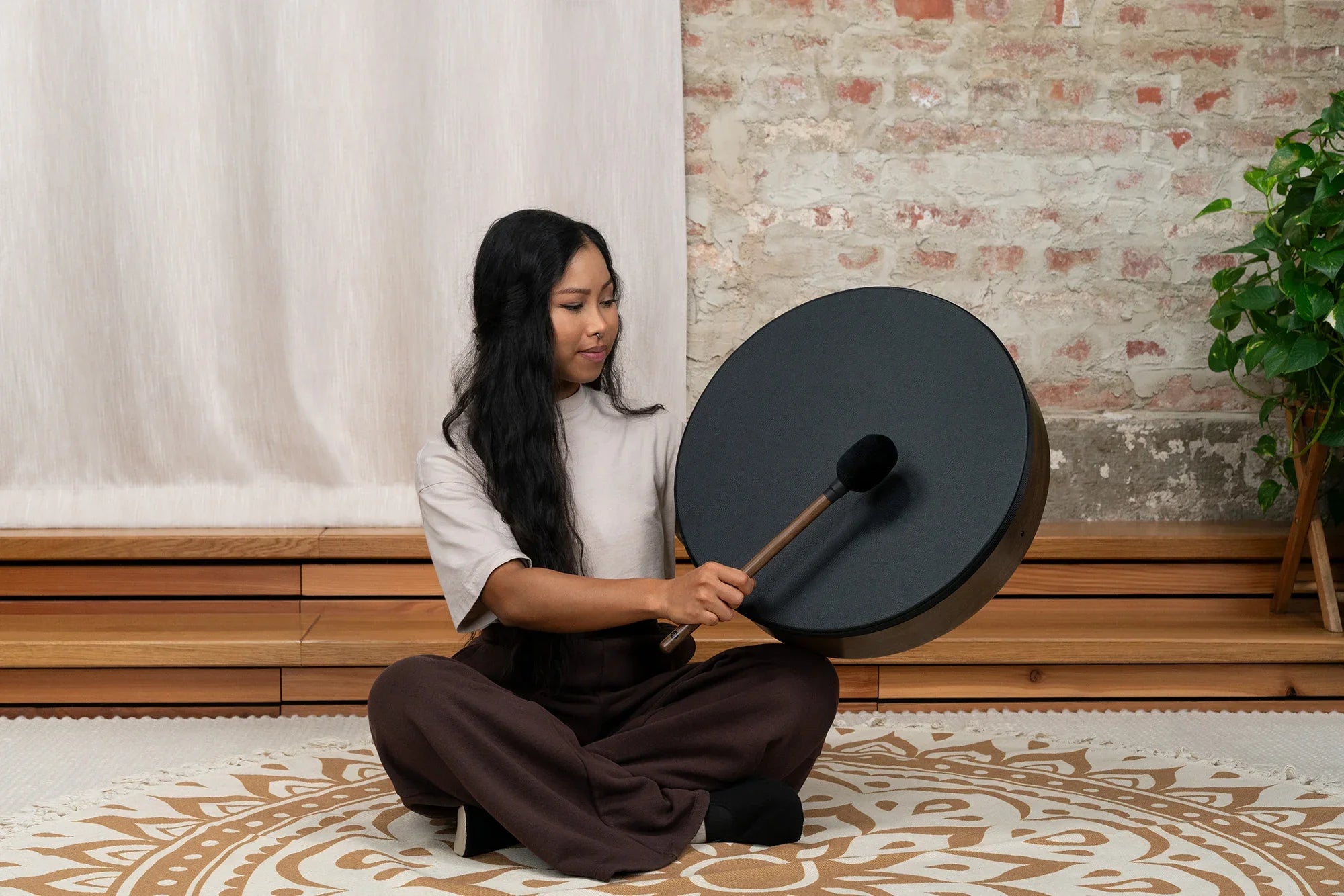 Woman playing a frame drum for sound healing in a peaceful indoor setting