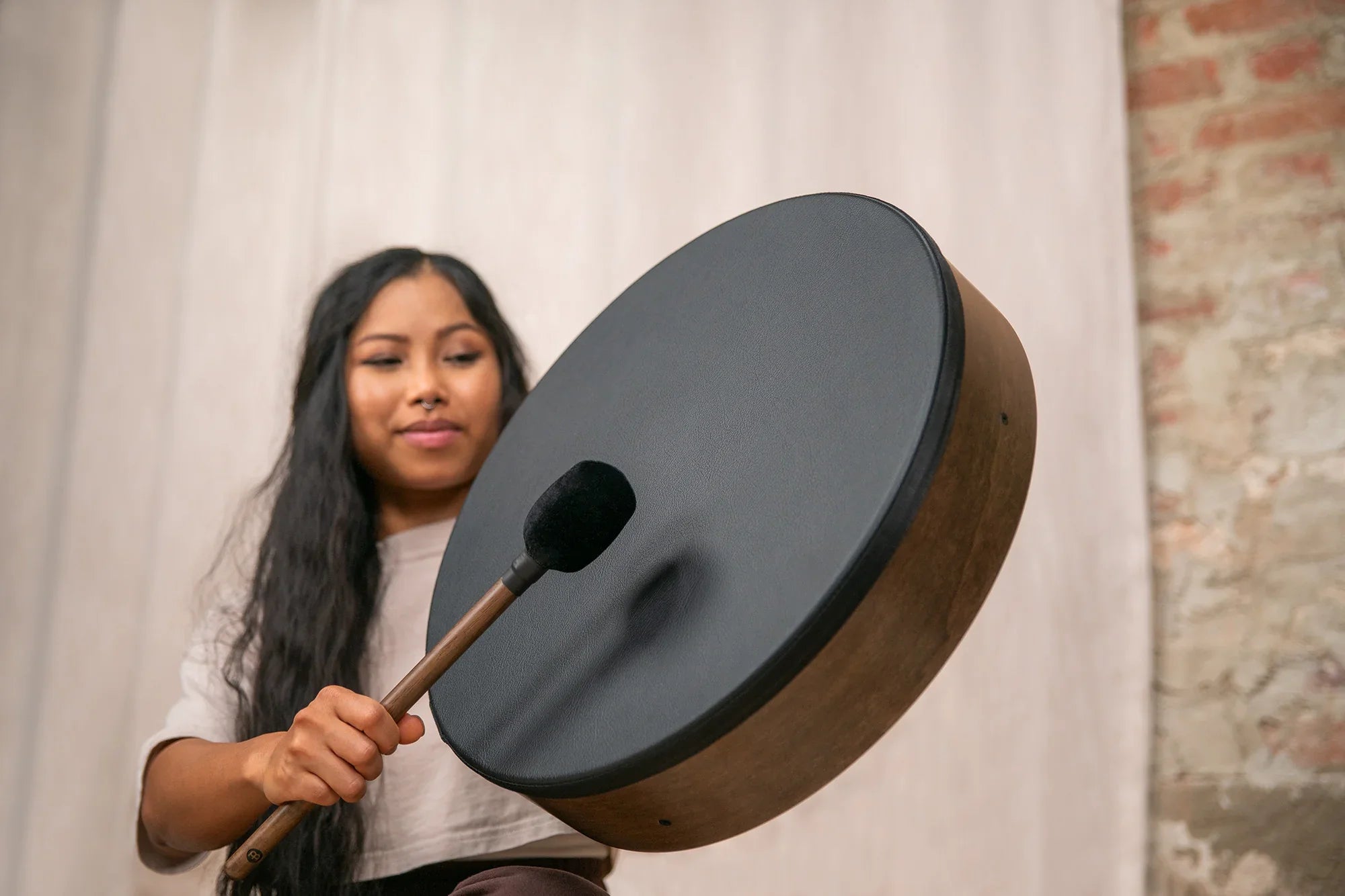 Woman playing a black frame drum with a mallet for sound healing