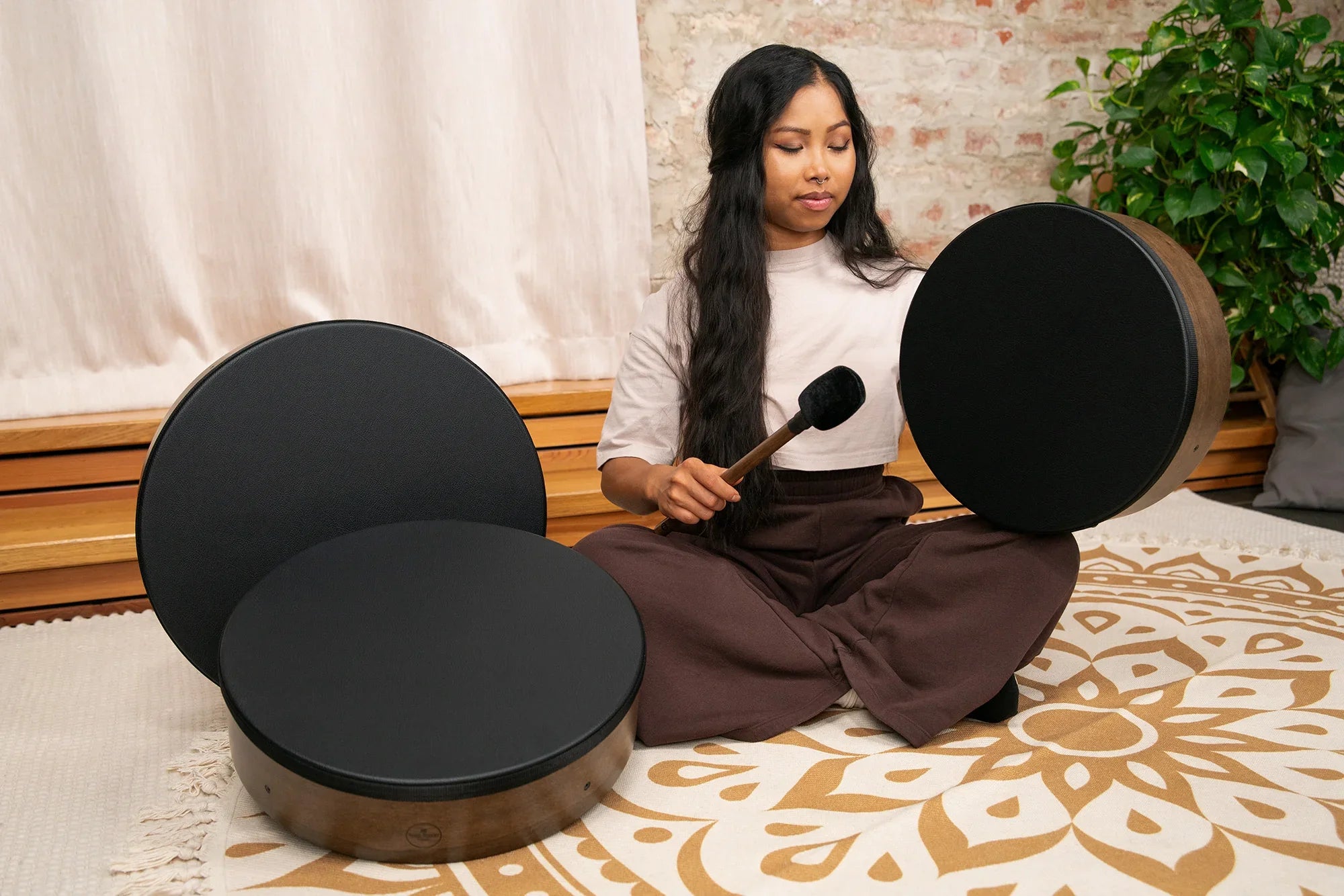 Woman playing black frame drum with mallet in a calming sound healing setting