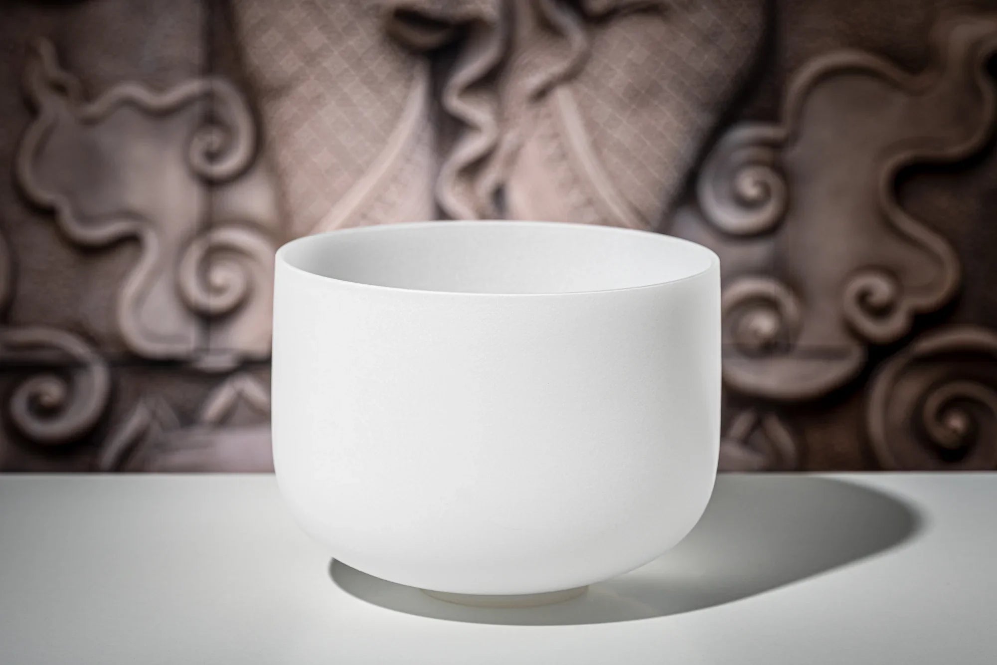 White crystal singing bowl for sound healing on a table with a decorative background