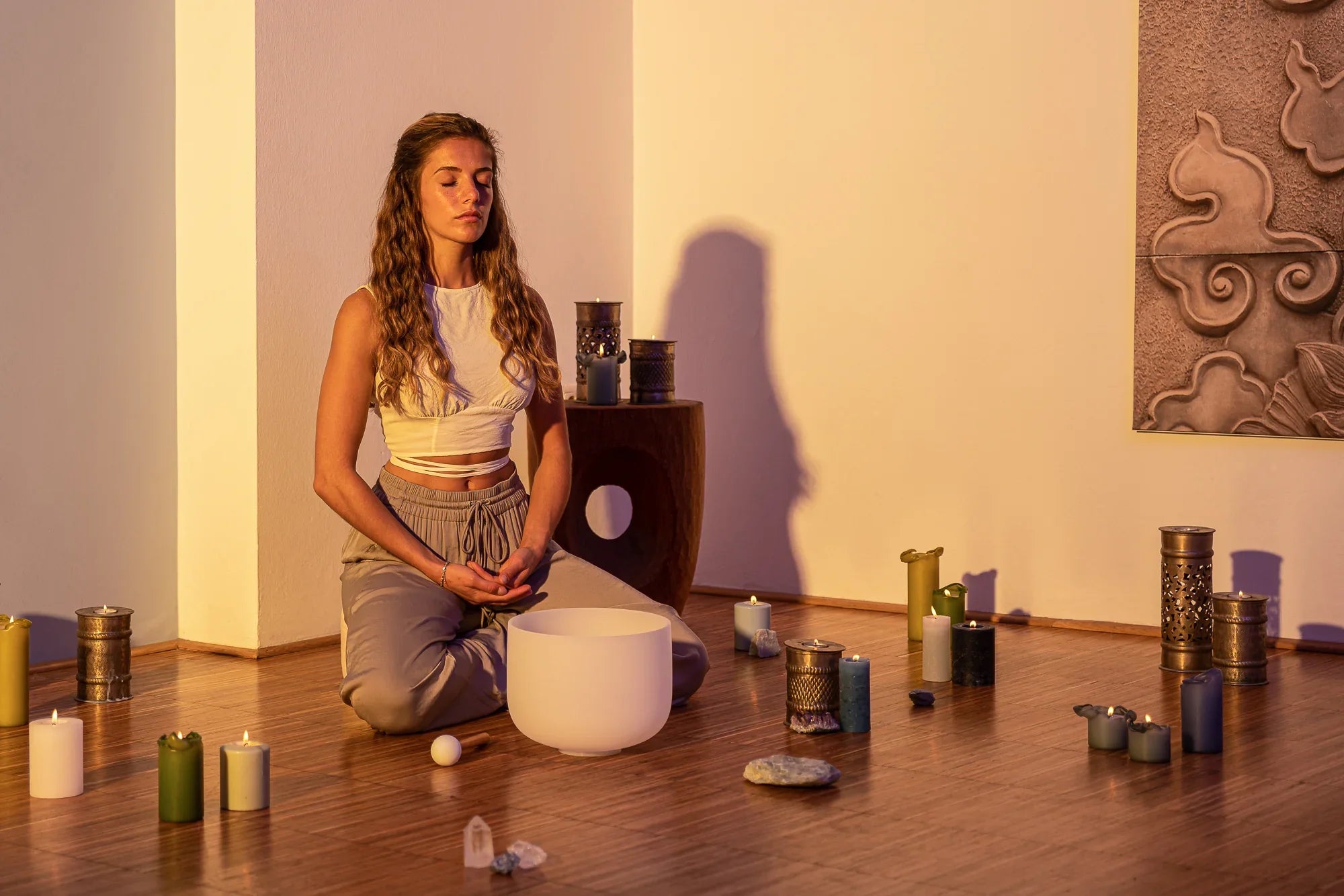 Woman meditating with crystal singing bowl, candles, and crystals in a calm room