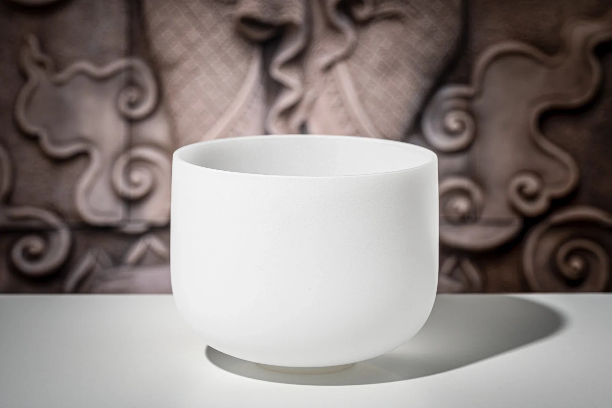 White crystal singing bowl for sound healing on a table with a decorative background
