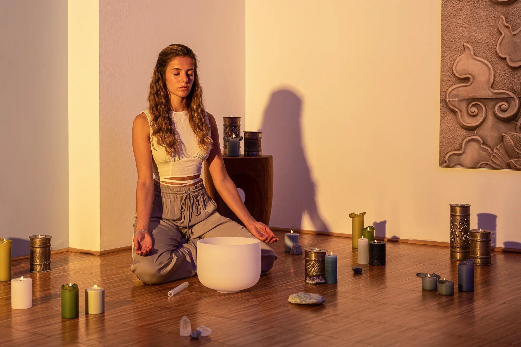 Woman meditating with a crystal singing bowl, candles, and healing crystals in a serene room