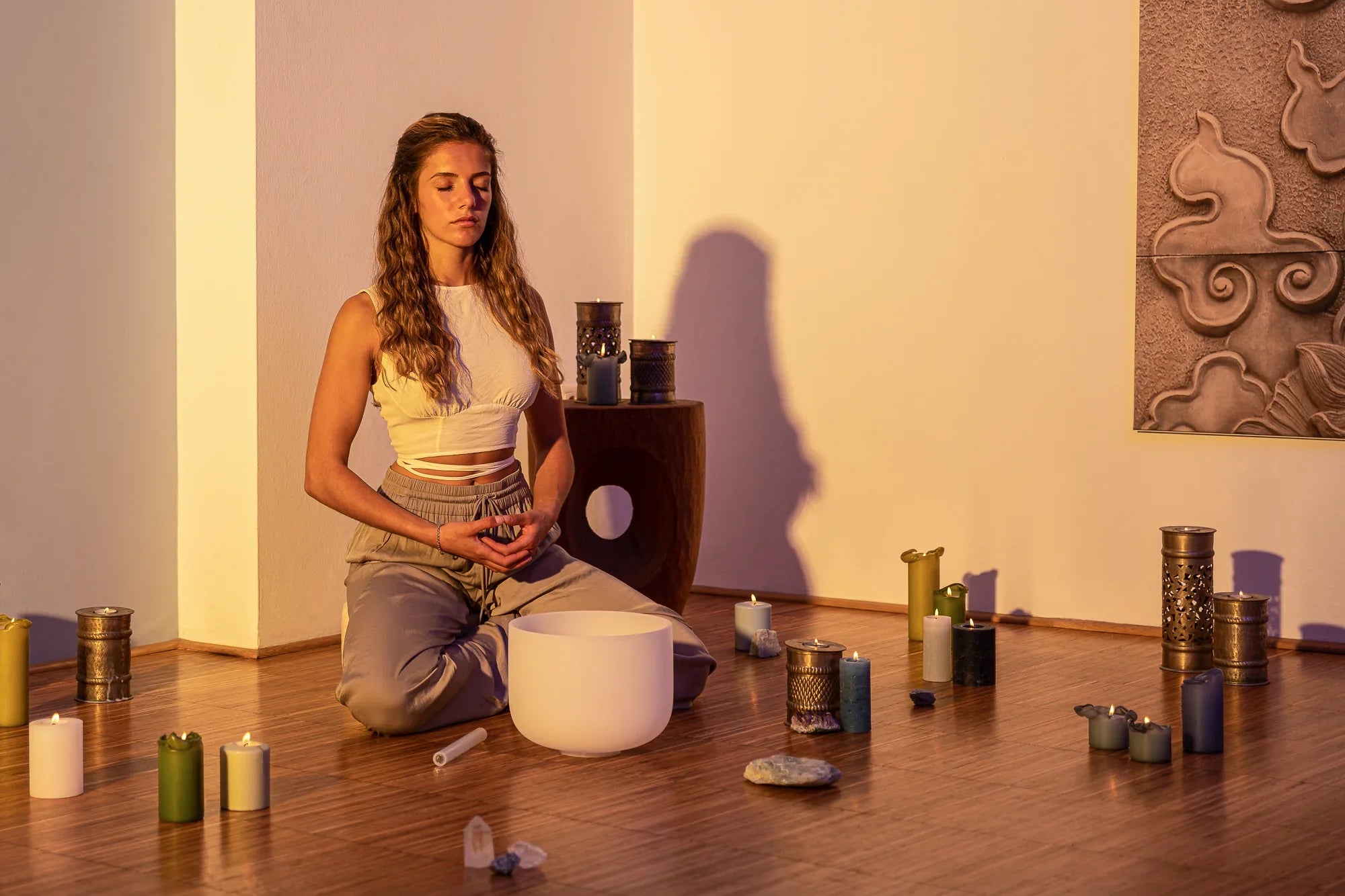 Woman meditating with crystal singing bowl, candles, and healing stones in a peaceful room