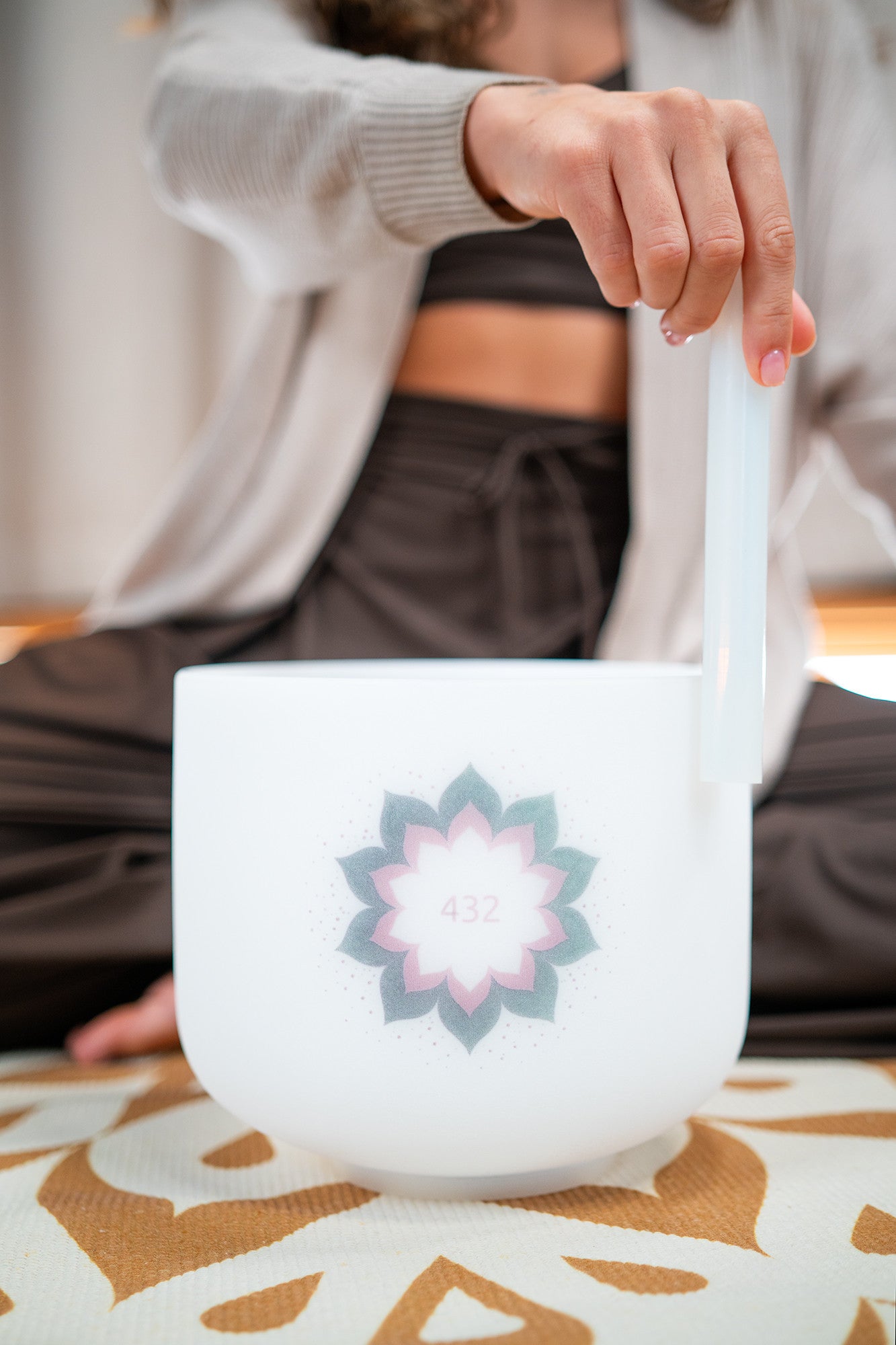 Person playing a white crystal singing bowl with a 432 Hz lotus design for sound healing