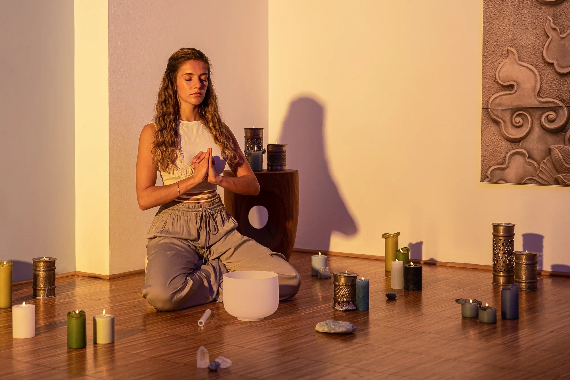 Woman meditating with a crystal singing bowl, surrounded by candles and healing stones