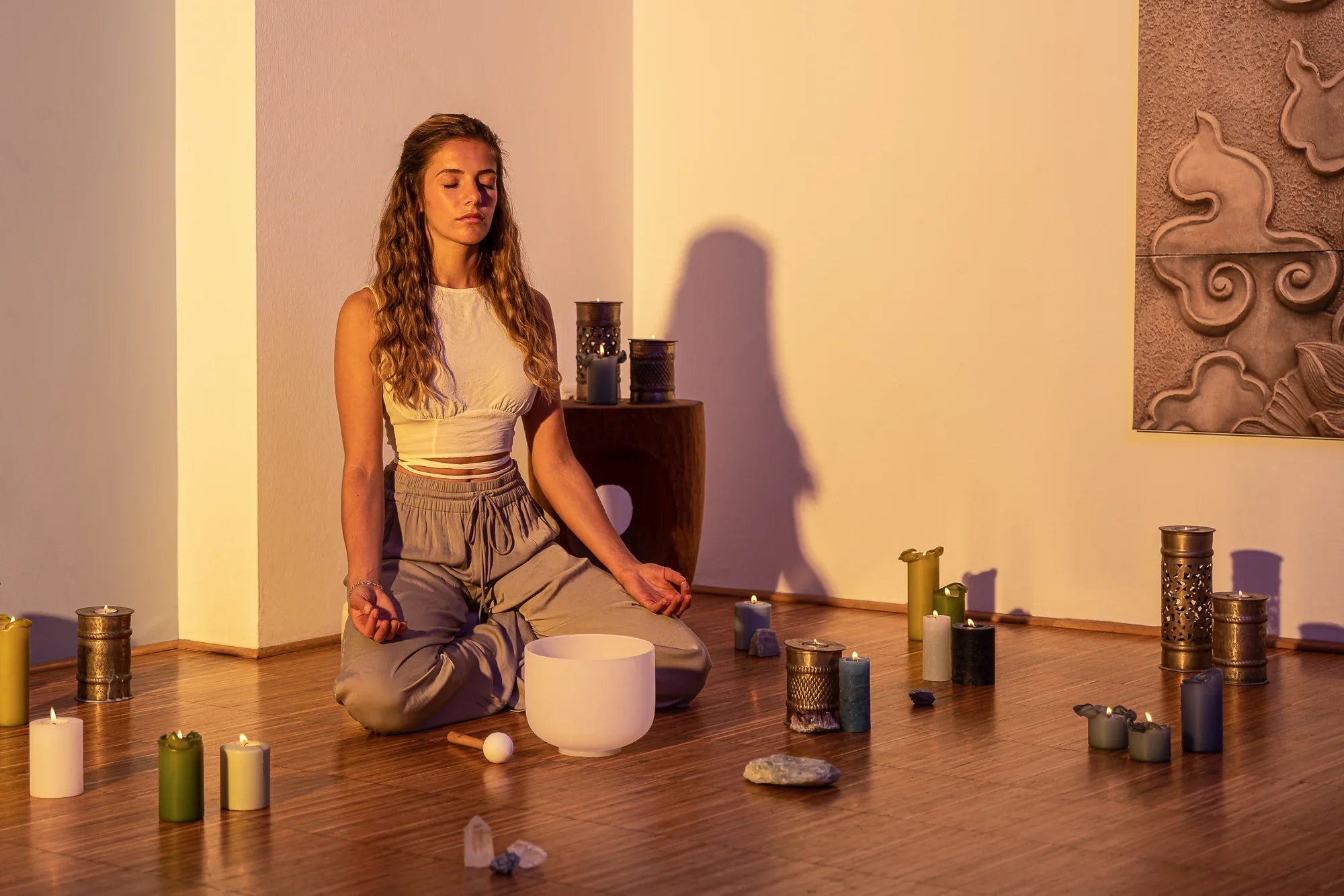 Woman meditating with a crystal singing bowl, candles, and healing crystals on wooden floor