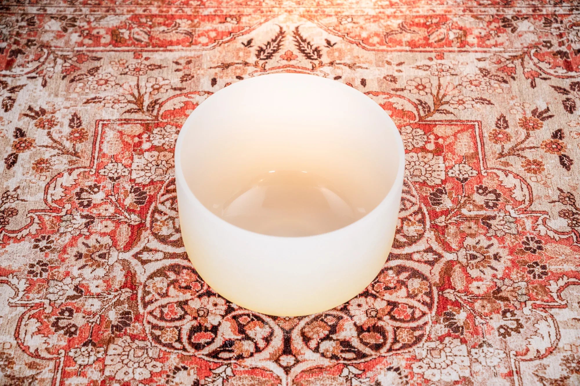 White crystal singing bowl on a patterned red and beige rug for sound healing
