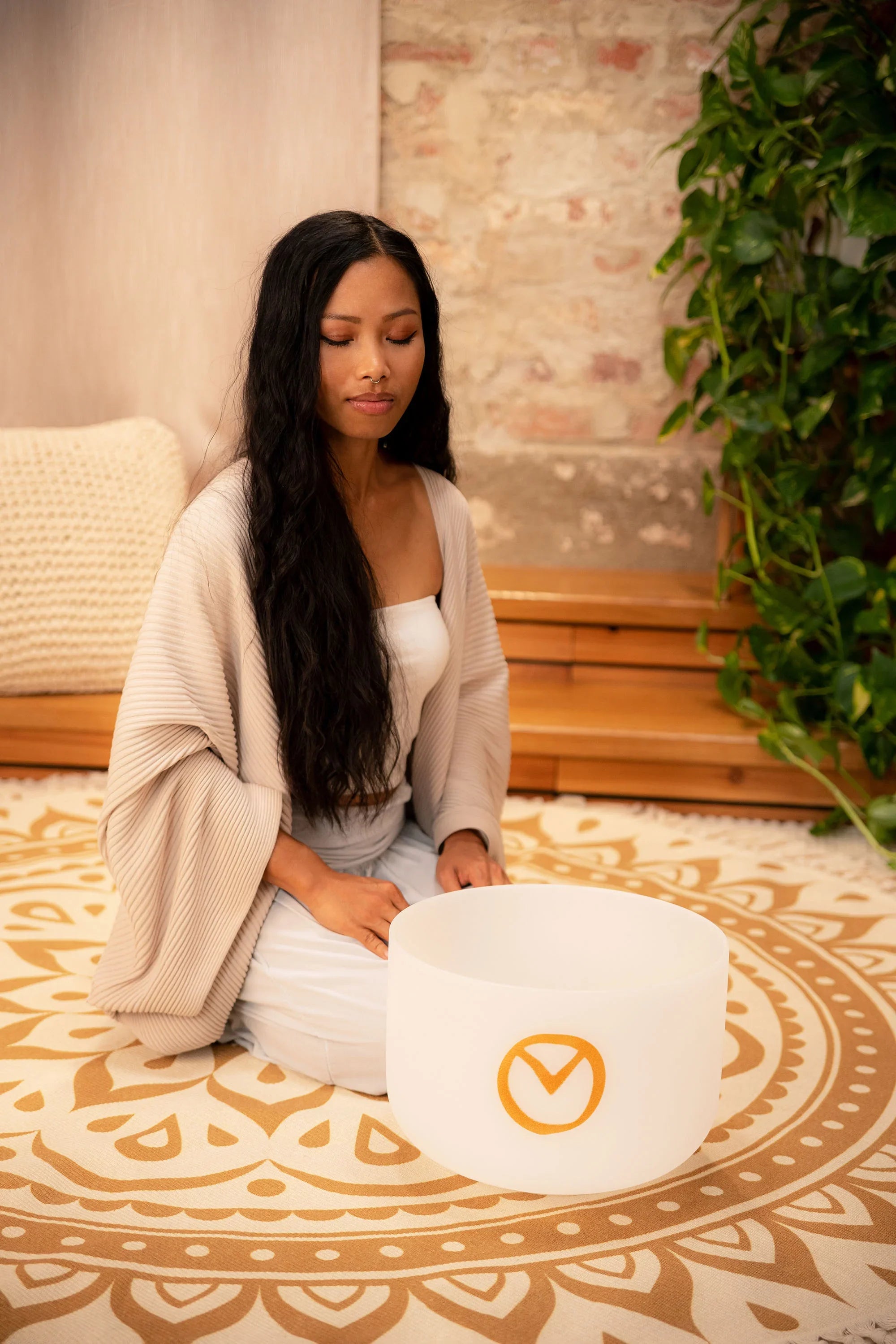 Woman meditating with a crystal singing bowl on a mandala rug in a peaceful room