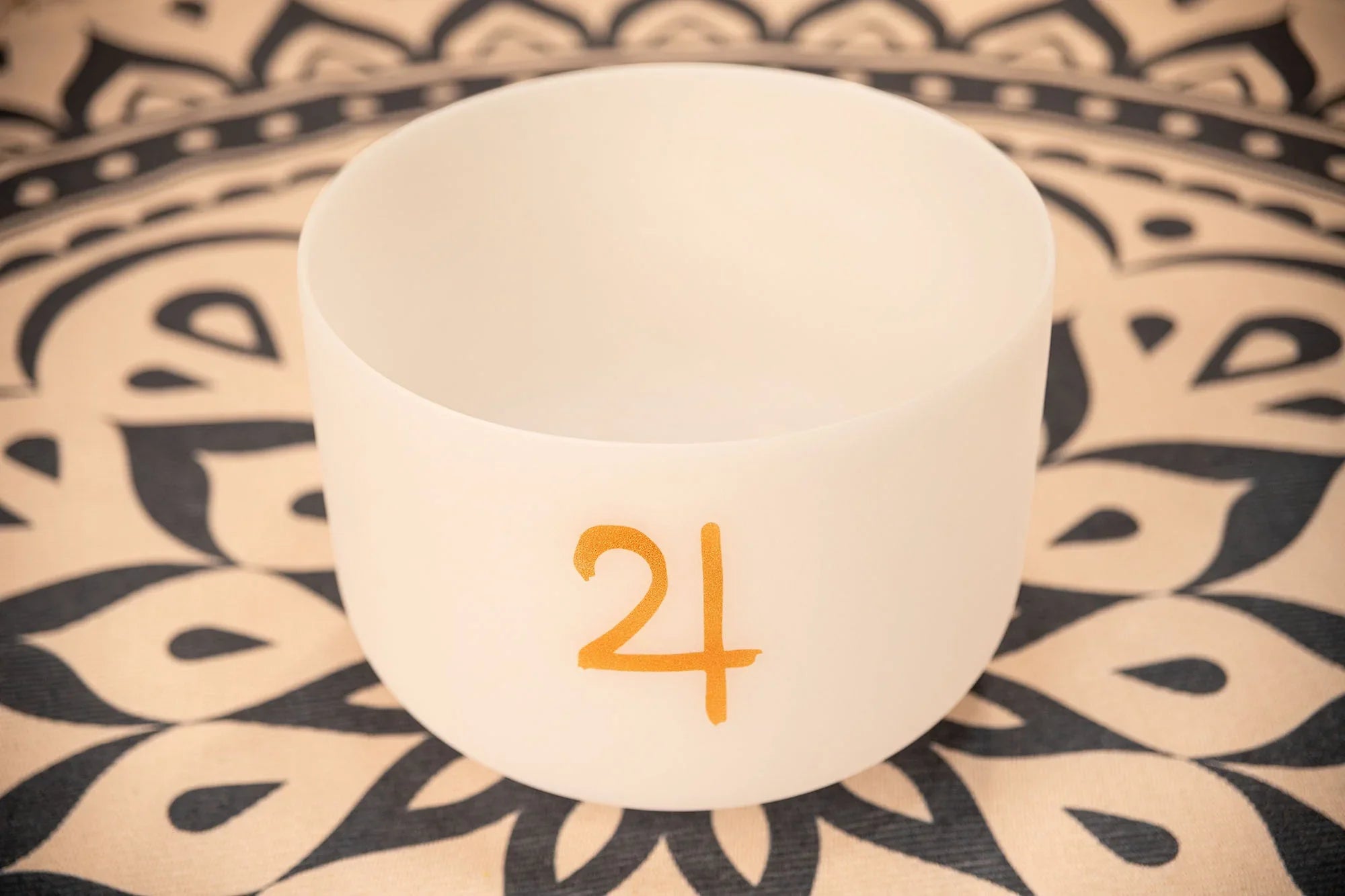 White crystal singing bowl with gold symbol on patterned mat for sound healing