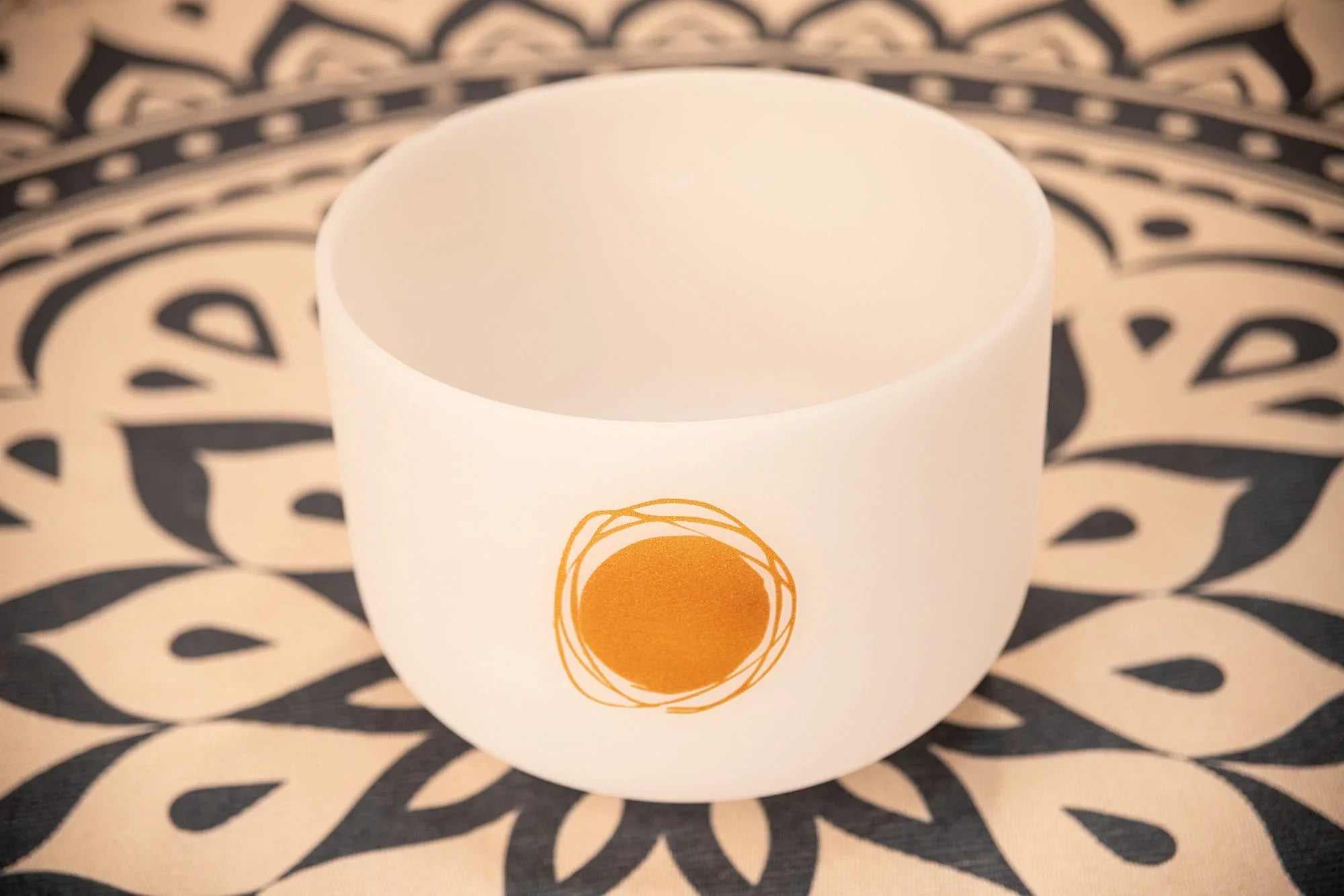 White crystal singing bowl with gold geometric design, on patterned cloth, sound healing instrument