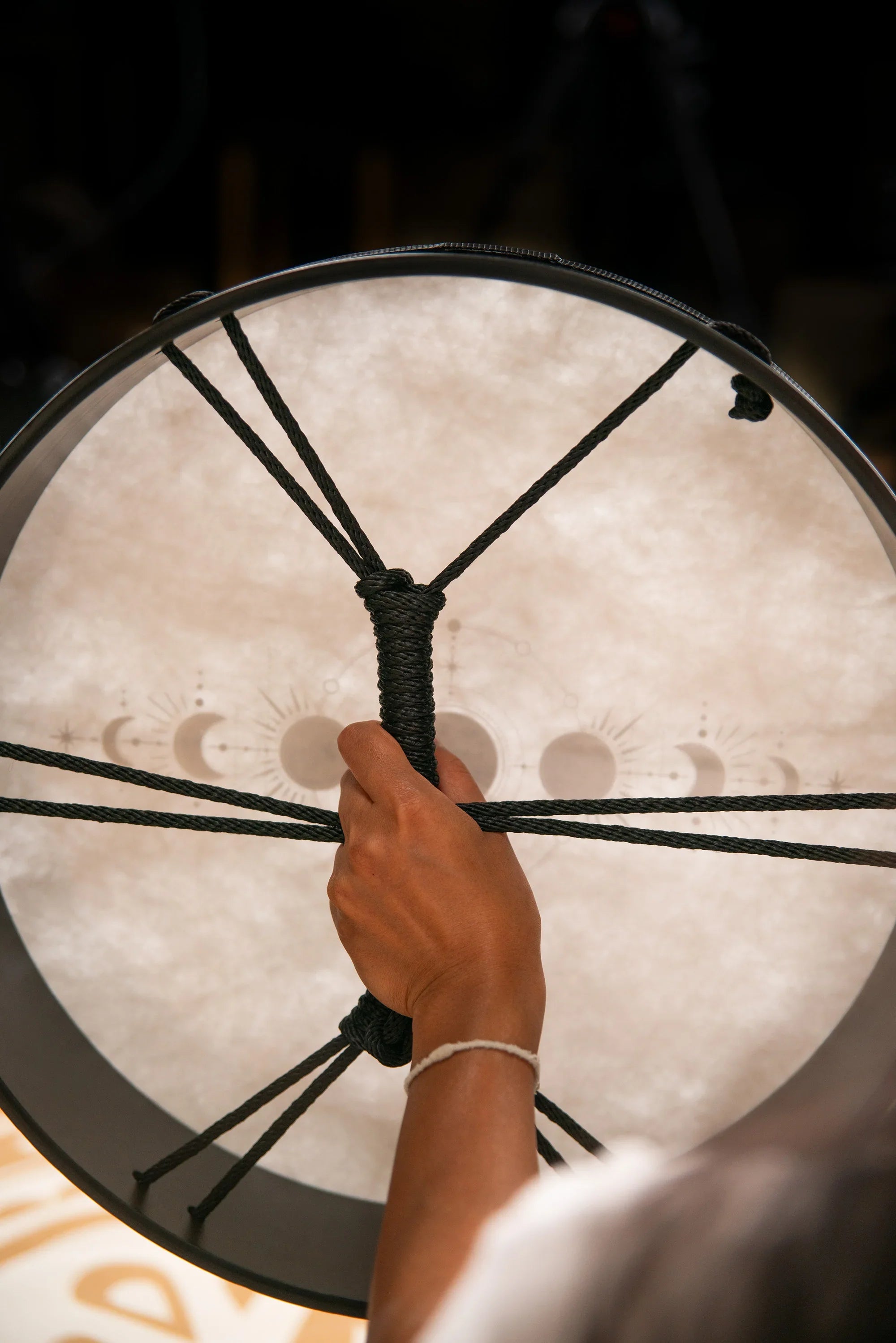 Hand holding a shamanic frame drum with moon phase design, energy healing instrument