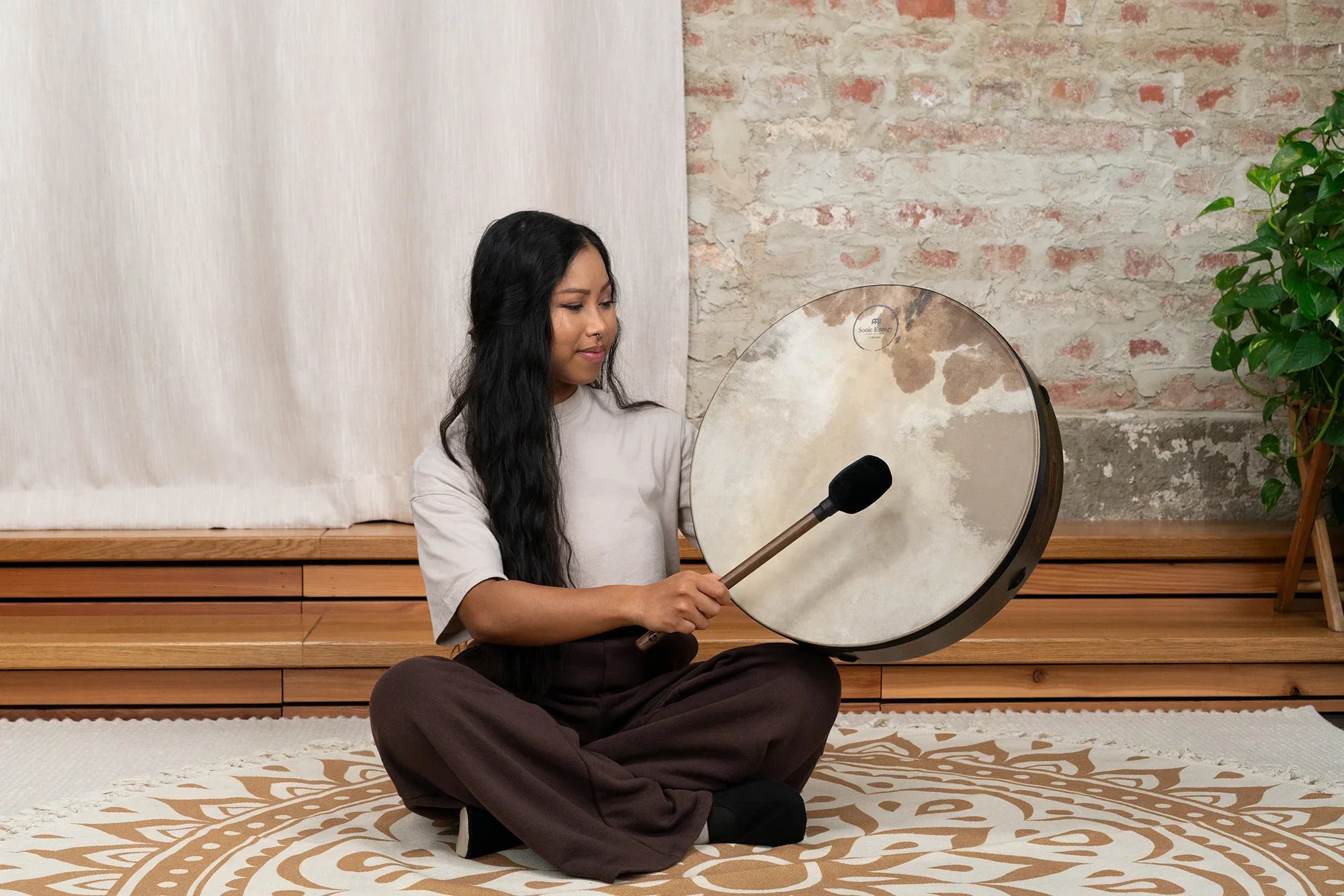 Woman playing large frame drum with mallet in serene, indoor sound healing setting