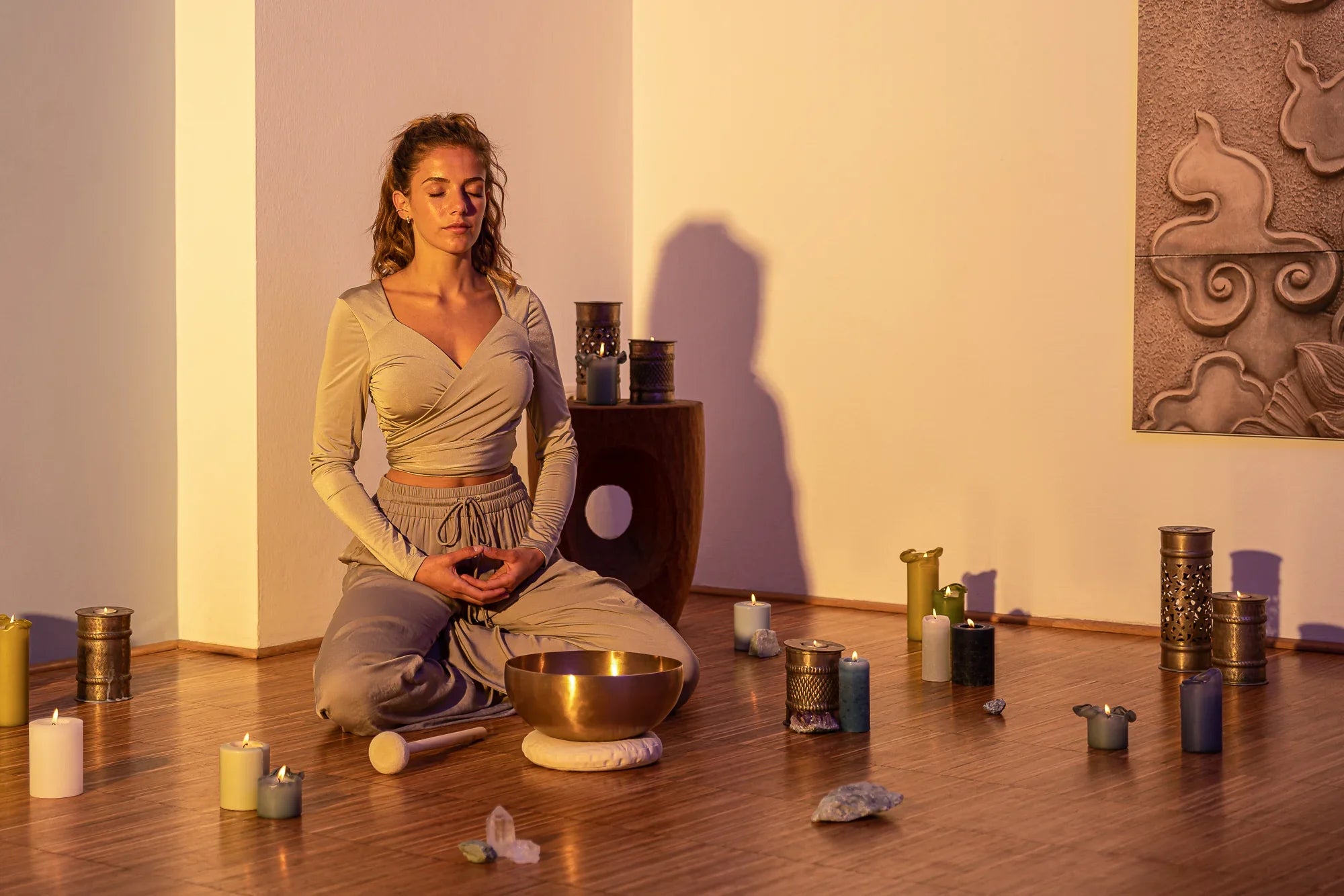 Woman meditating with singing bowl, candles, and crystals in a peaceful sound healing space