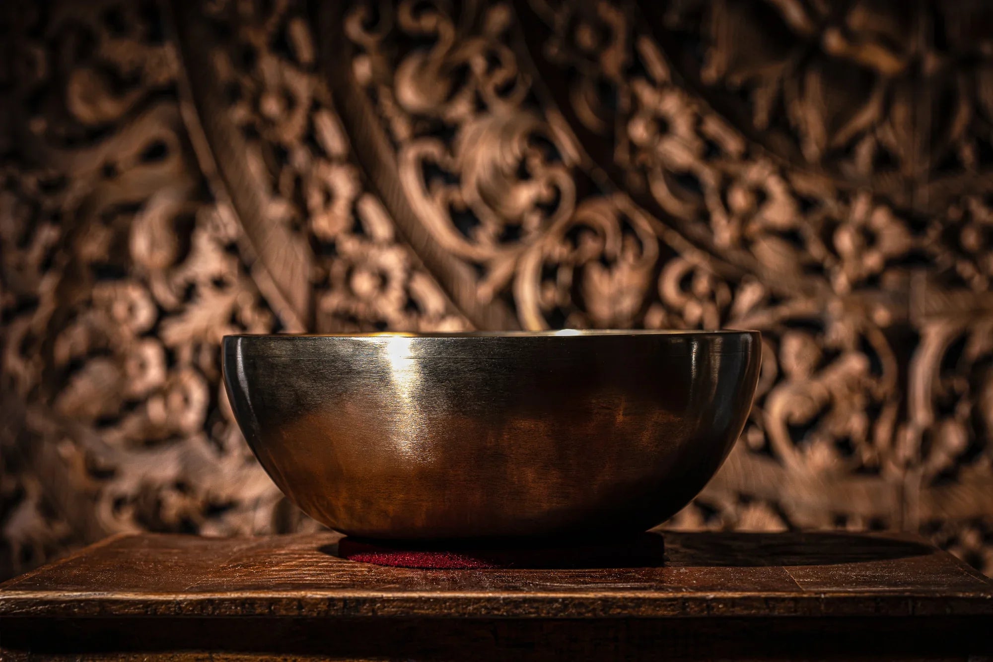 Metal singing bowl for sound healing on wooden table with ornate carved background