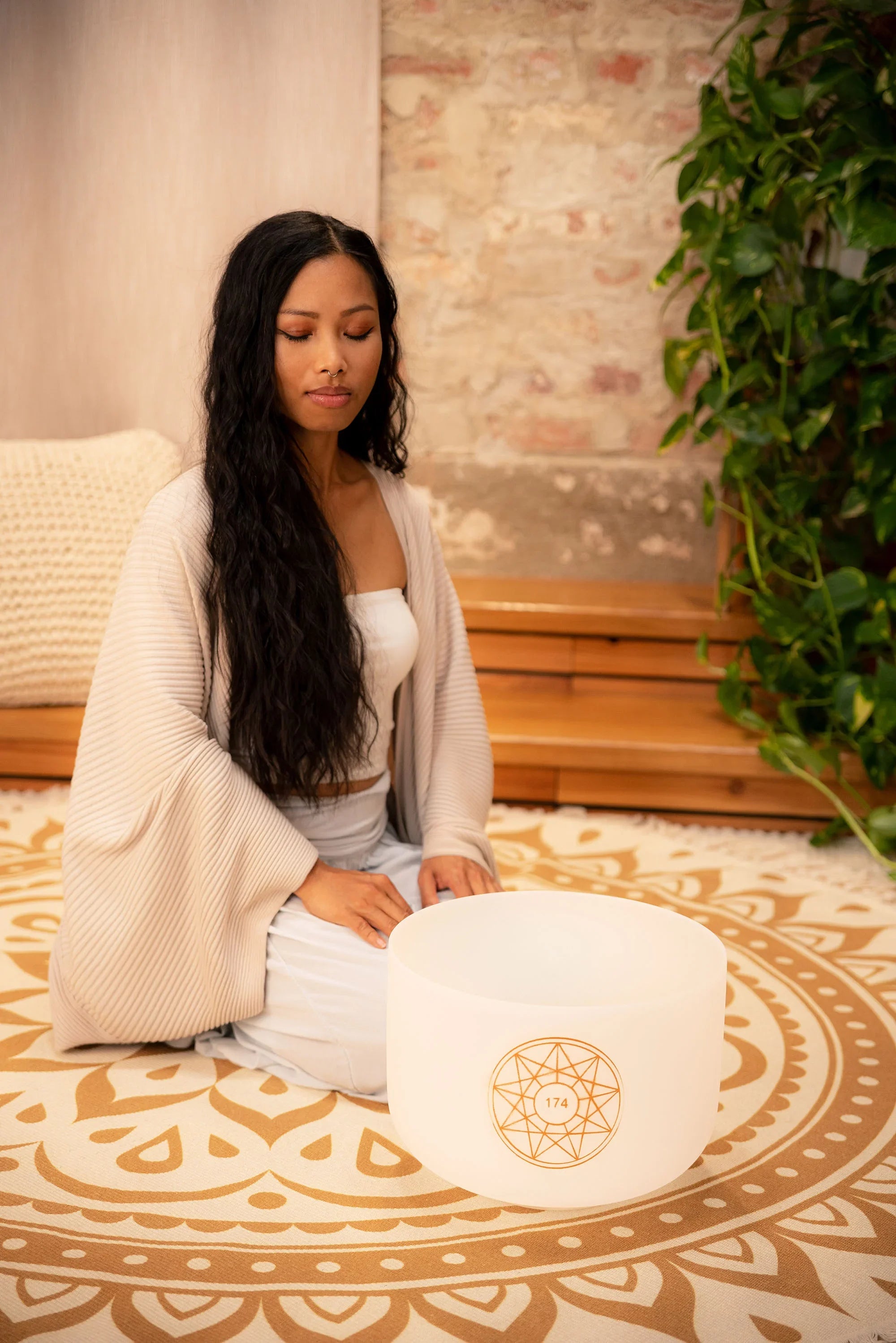 Woman meditating indoors with a white crystal singing bowl on a patterned rug