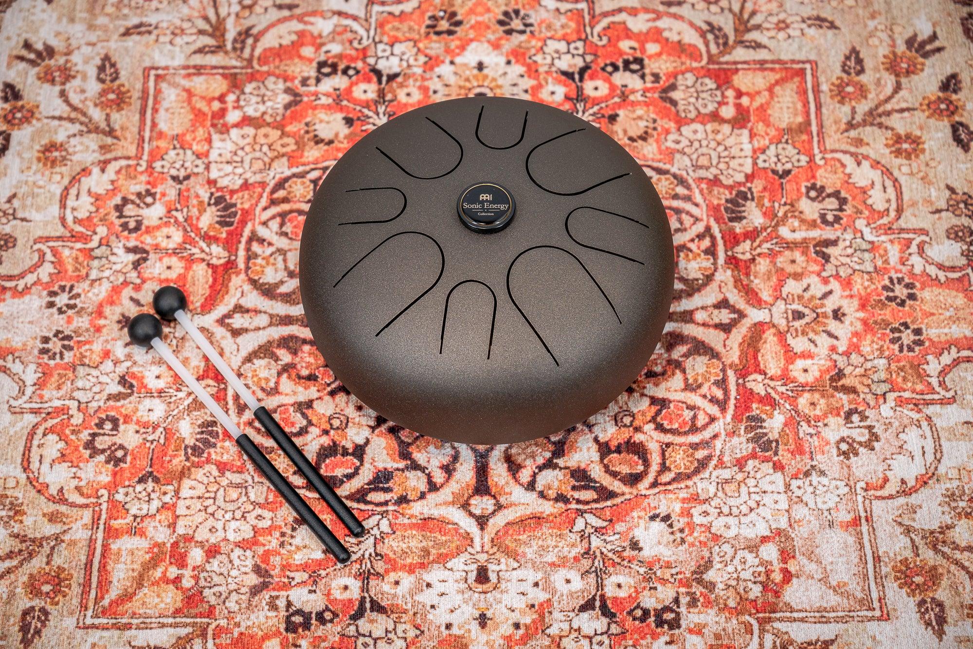 Steel tongue drum and mallets on a decorative patterned rug, sound healing instrument