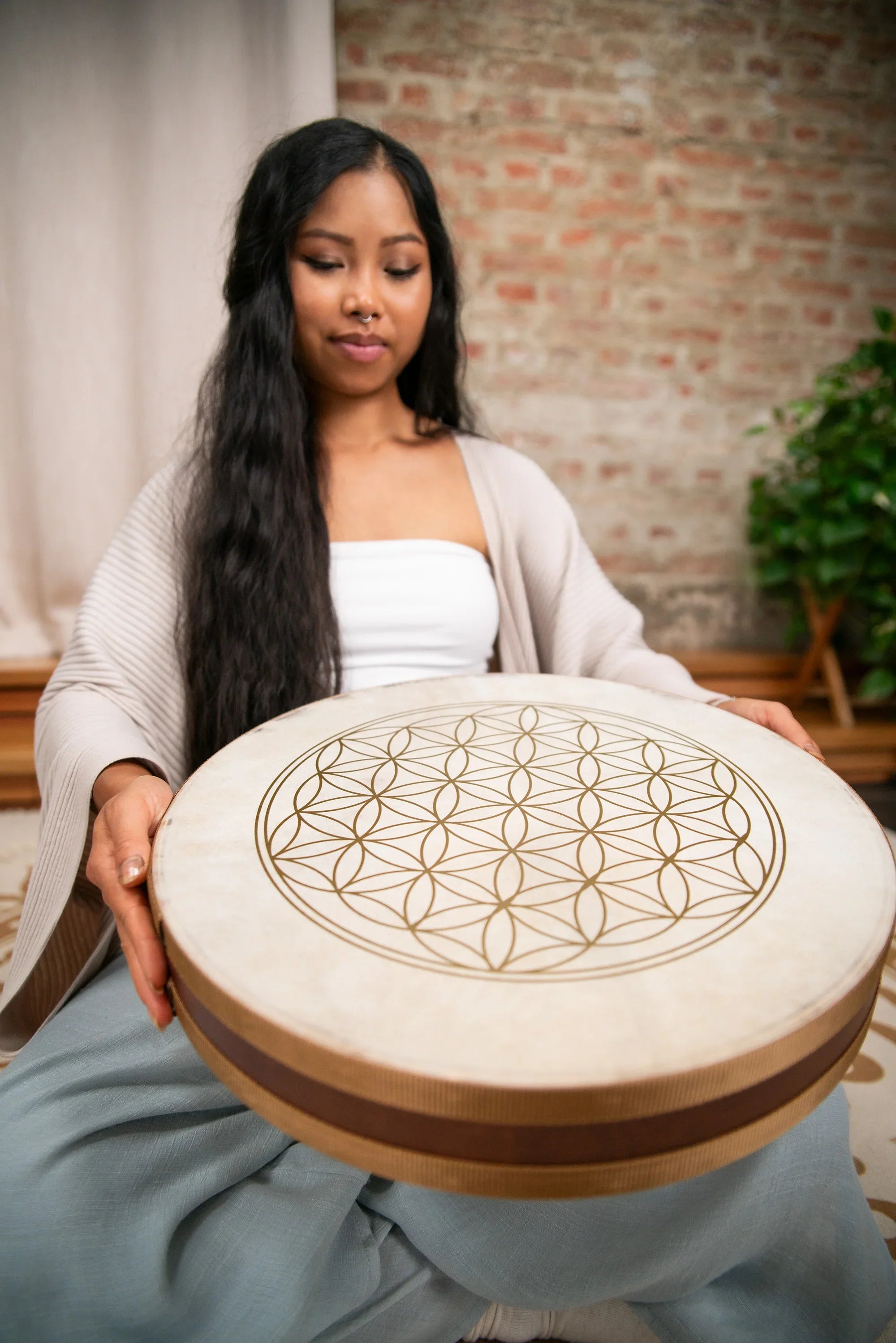 Woman holding a large frame drum with geometric flower of life design in a peaceful room