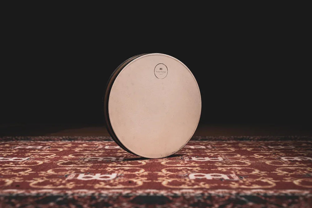 Frame drum for sound healing on patterned rug in warm, ambient lighting
