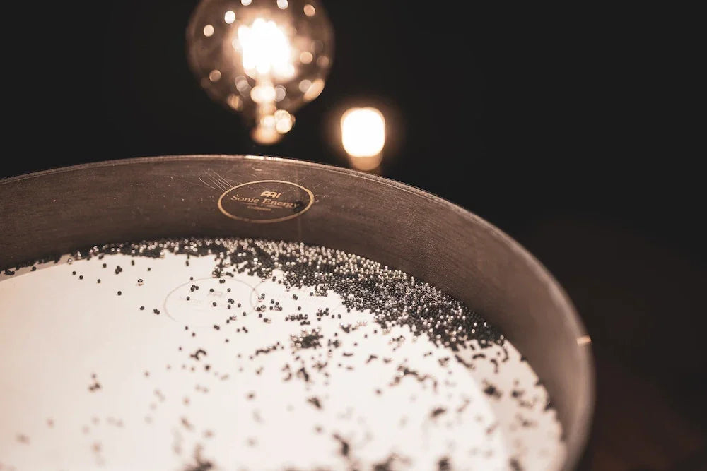 Chladni plate sound healing instrument with black granules, warm lighting in background
