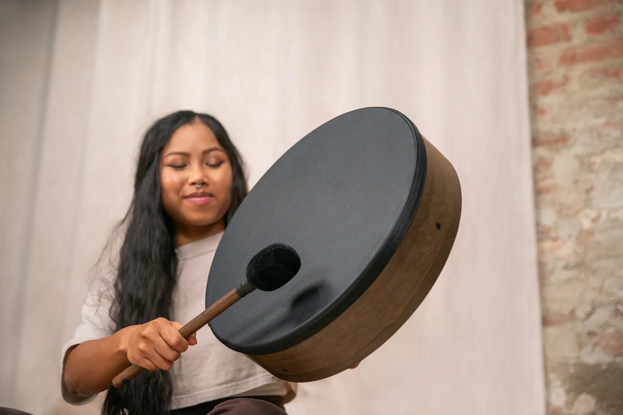 Woman playing a black frame drum with mallet in an indoor sound healing setting