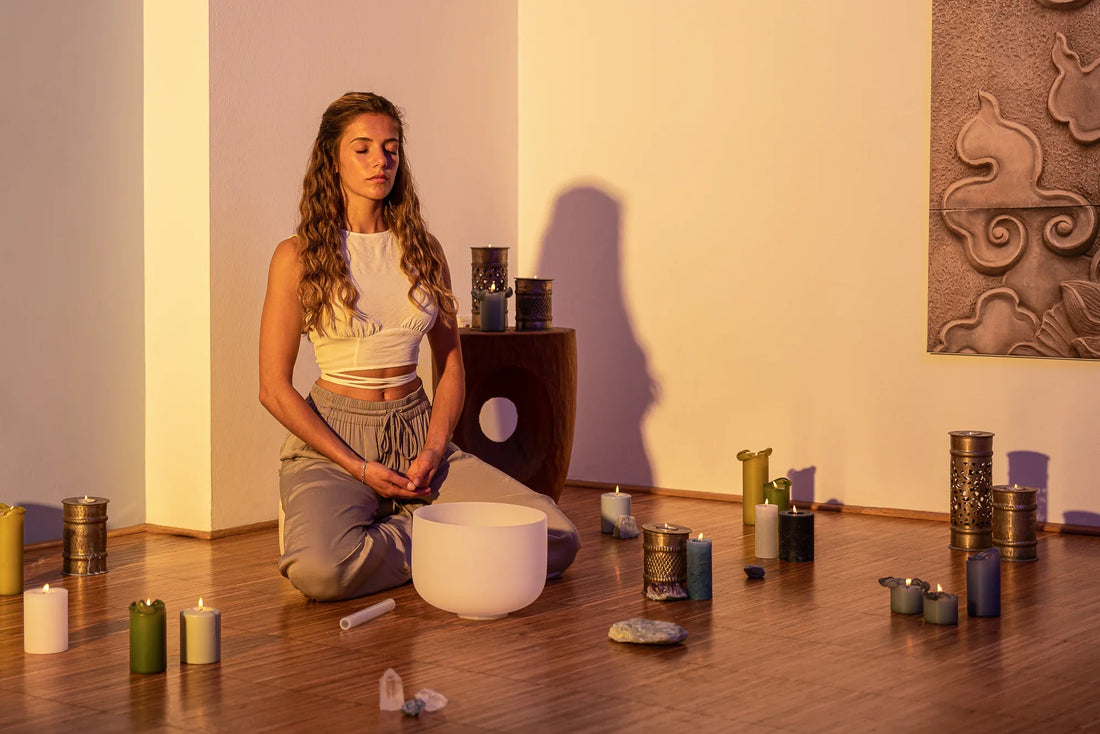 Woman meditating with a crystal singing bowl surrounded by candles and crystals in a serene room