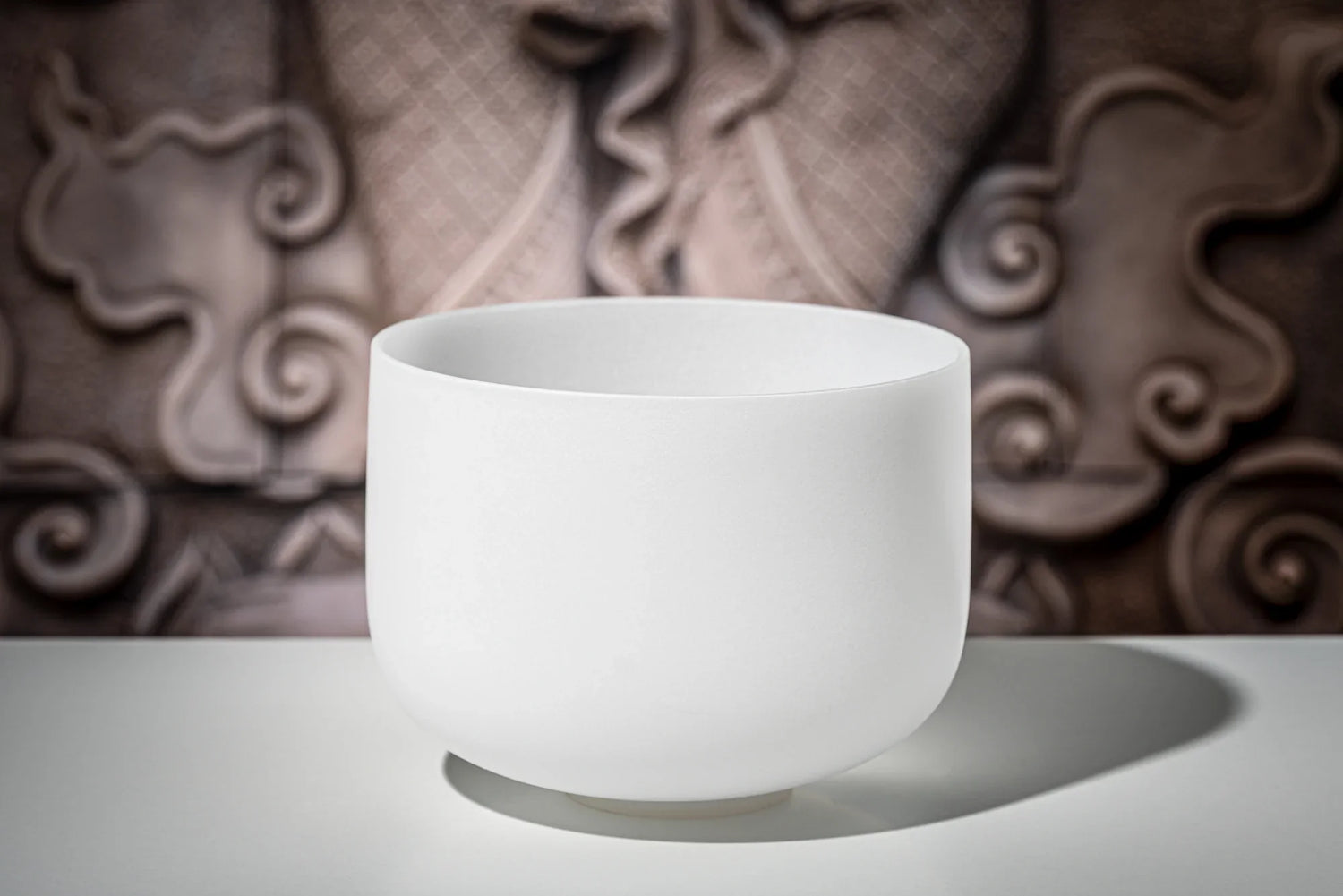 White crystal singing bowl for sound healing on a table with a decorative background