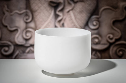 White crystal singing bowl for sound healing on a table with a decorative background