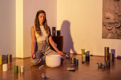 Woman meditating with a crystal singing bowl, candles, and healing crystals in a serene room