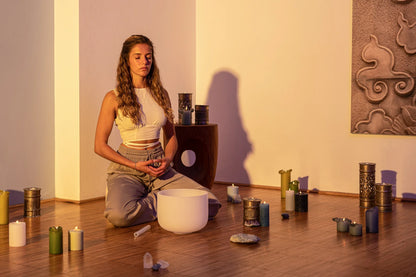 Woman meditating with crystal singing bowl, candles, and healing stones in a peaceful room
