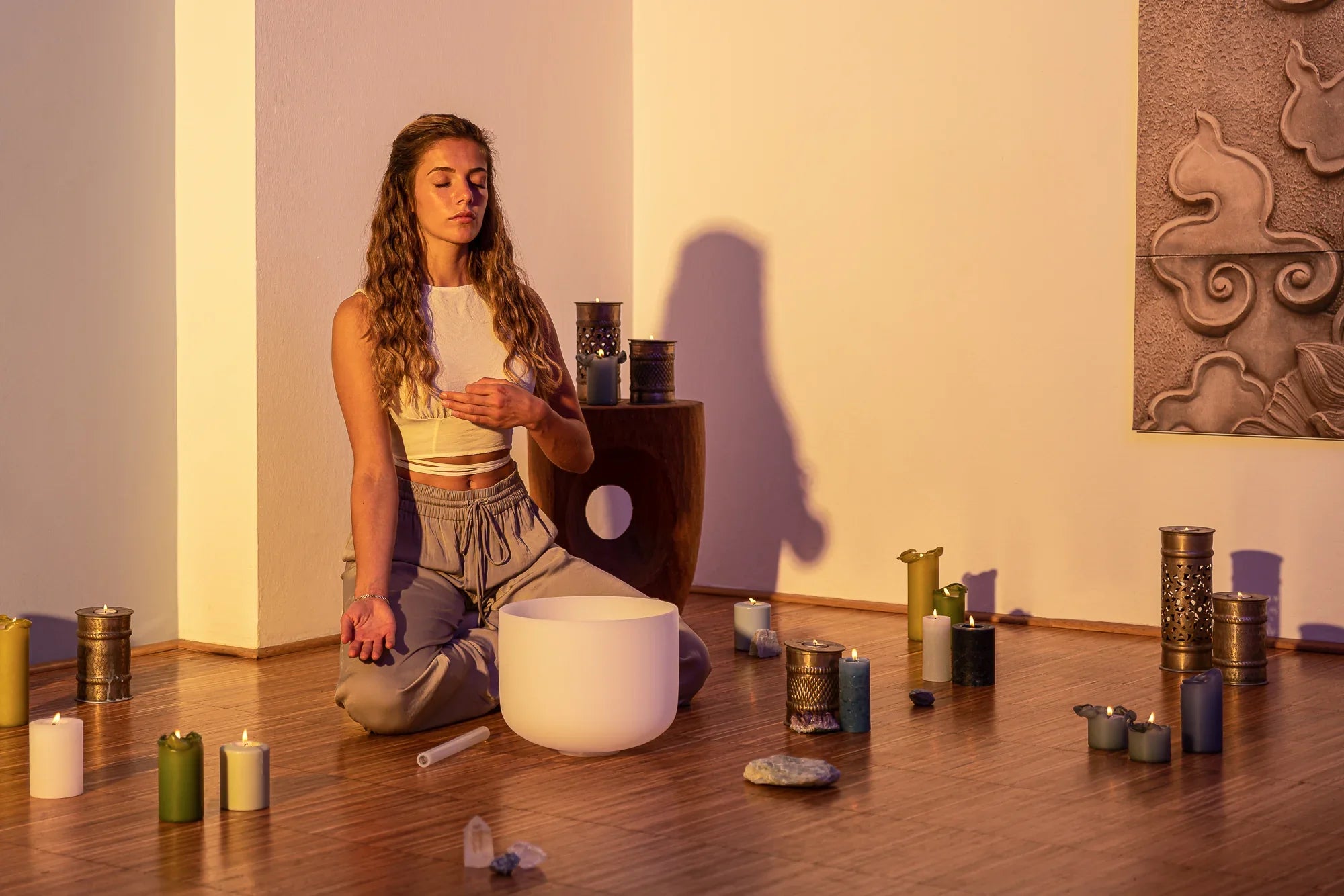 Woman meditating with a crystal singing bowl, candles, and crystals in a peaceful room