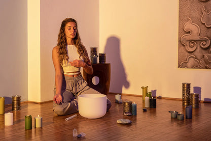 Woman meditating with a crystal singing bowl, candles, and crystals in a peaceful room