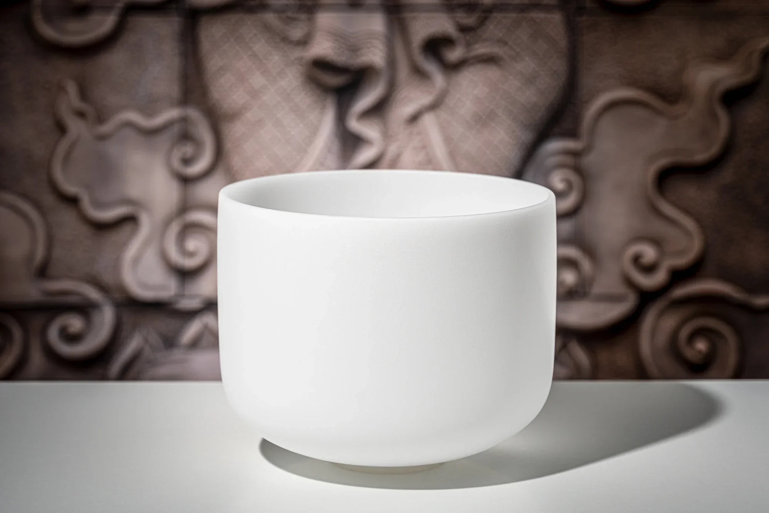White crystal singing bowl for sound healing on a table, ornate carved background