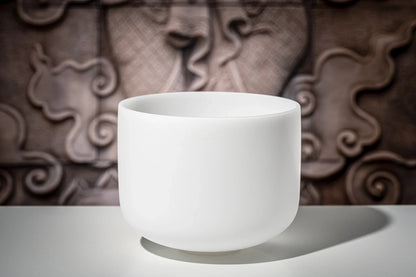 White crystal singing bowl for sound healing on a table, ornate carved background