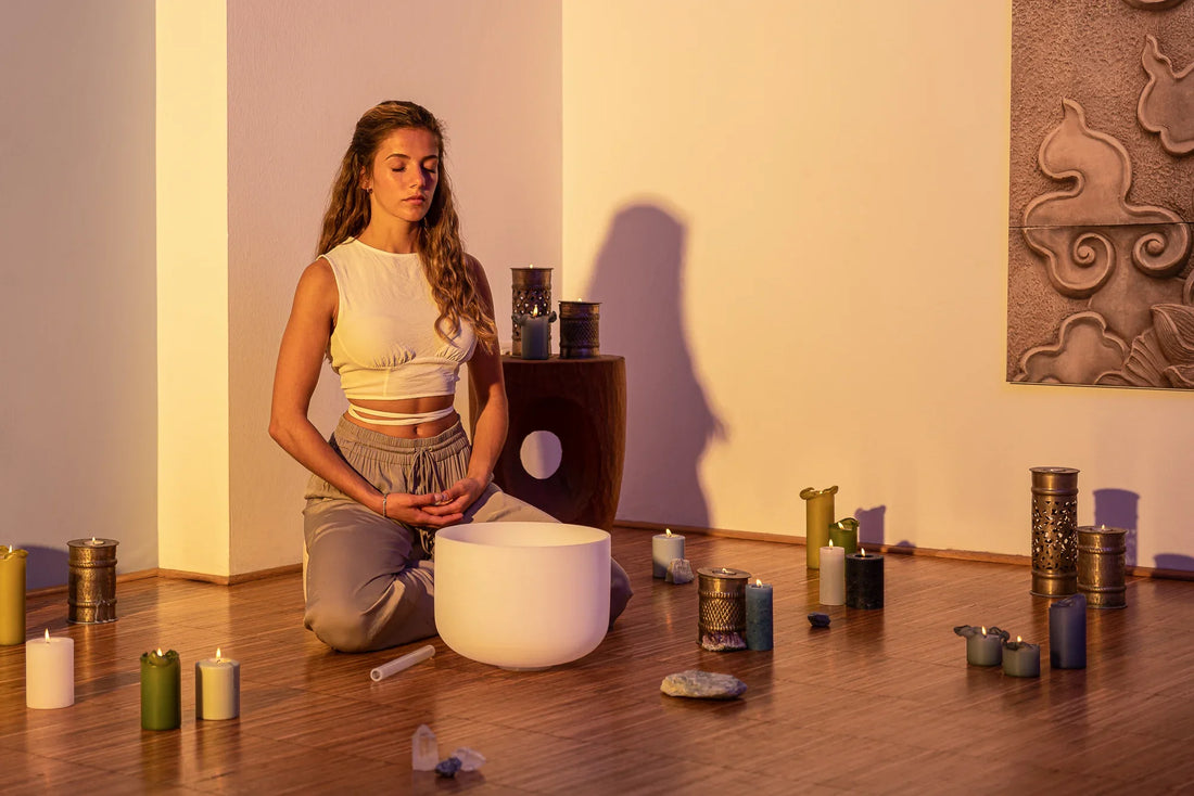 Woman meditating with crystal singing bowl, candles, and crystals in a calming room