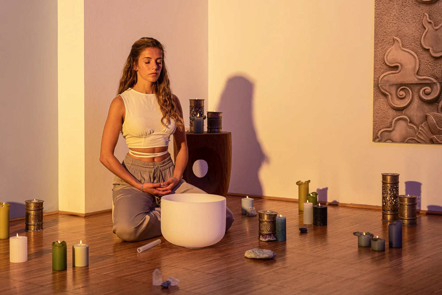 Woman meditating with crystal singing bowl, candles, and crystals in a calming room