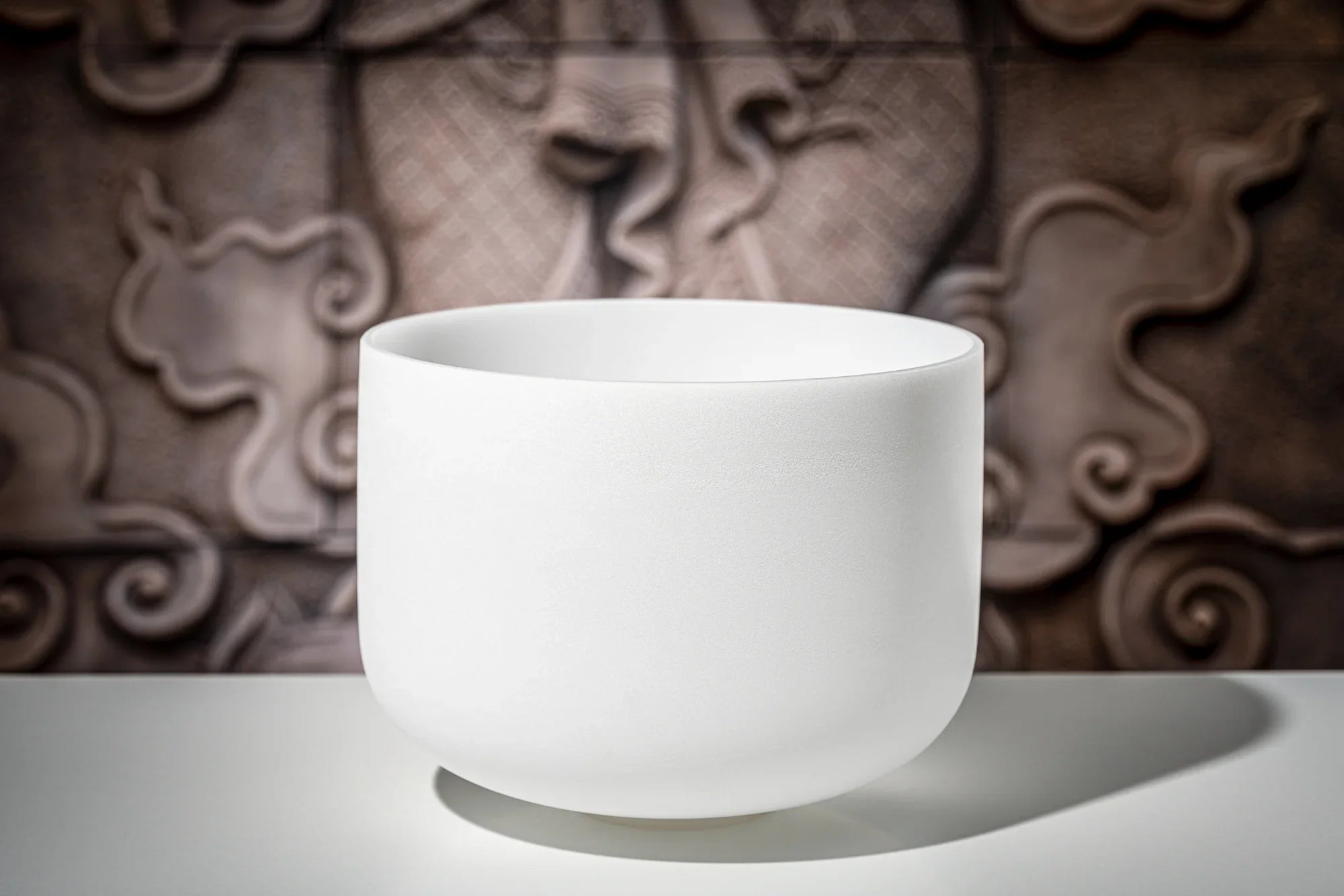 White crystal singing bowl for sound healing on table with artistic background