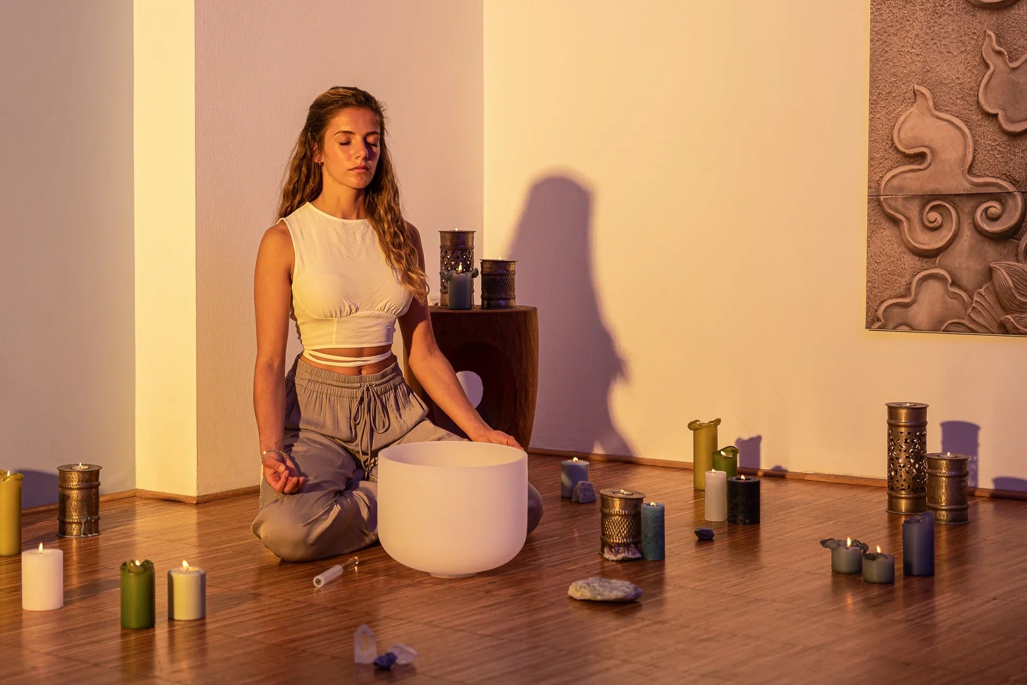 Woman meditating with crystal singing bowl, candles, and crystals in a serene room