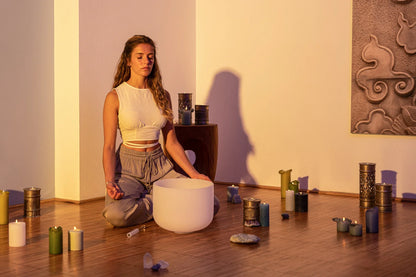 Woman meditating with crystal singing bowl, candles, and crystals in a serene room