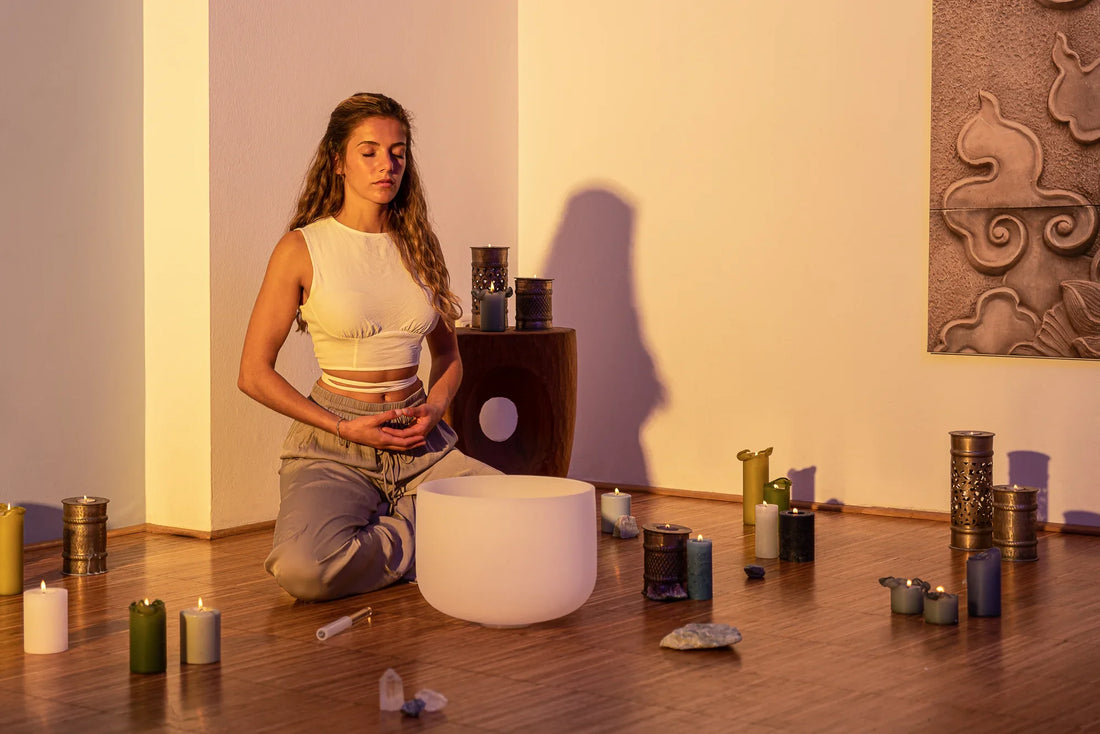 Woman meditating with a crystal singing bowl, crystals, and candles in a calming room