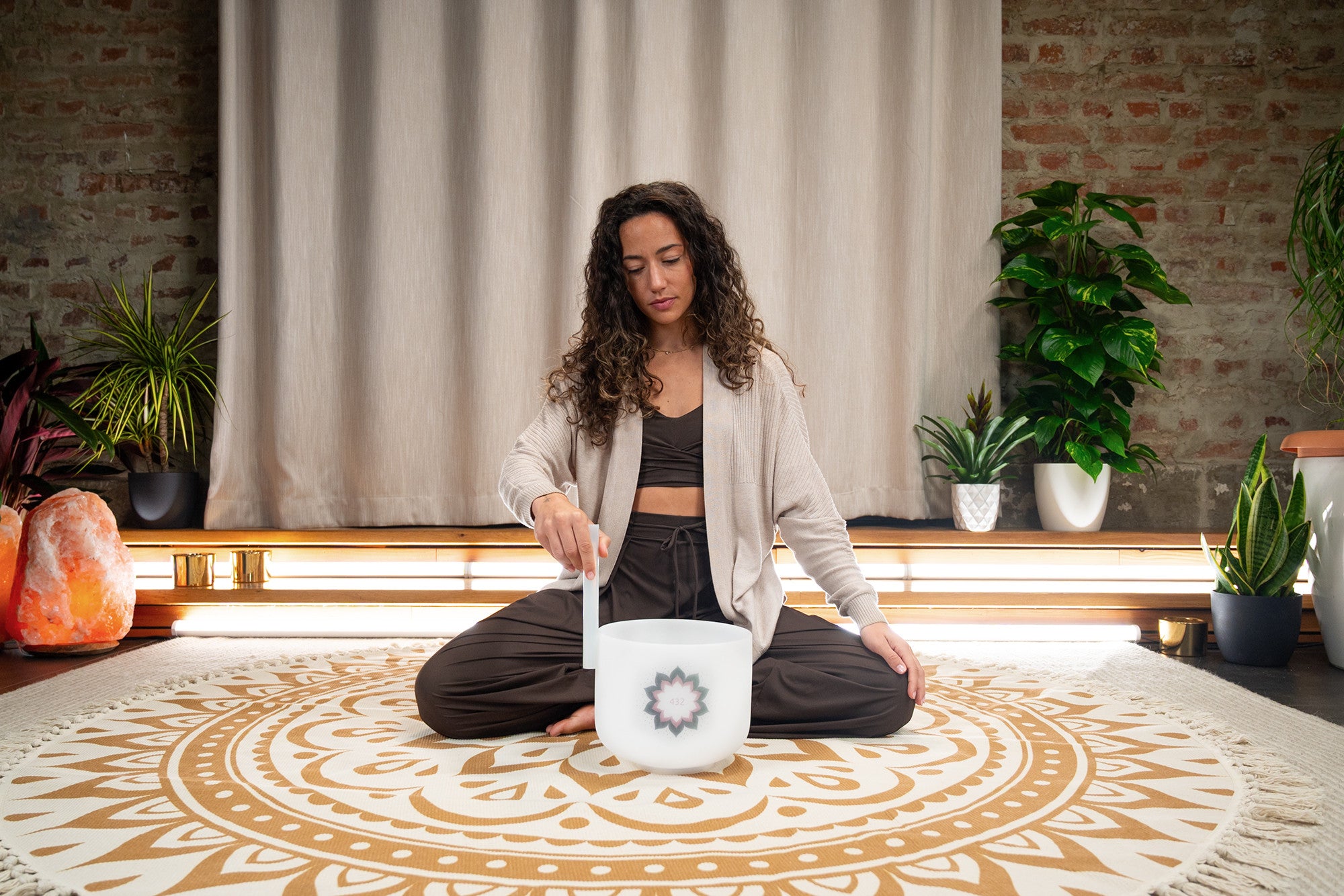 Woman practicing sound healing with a crystal singing bowl on a mandala yoga mat indoors