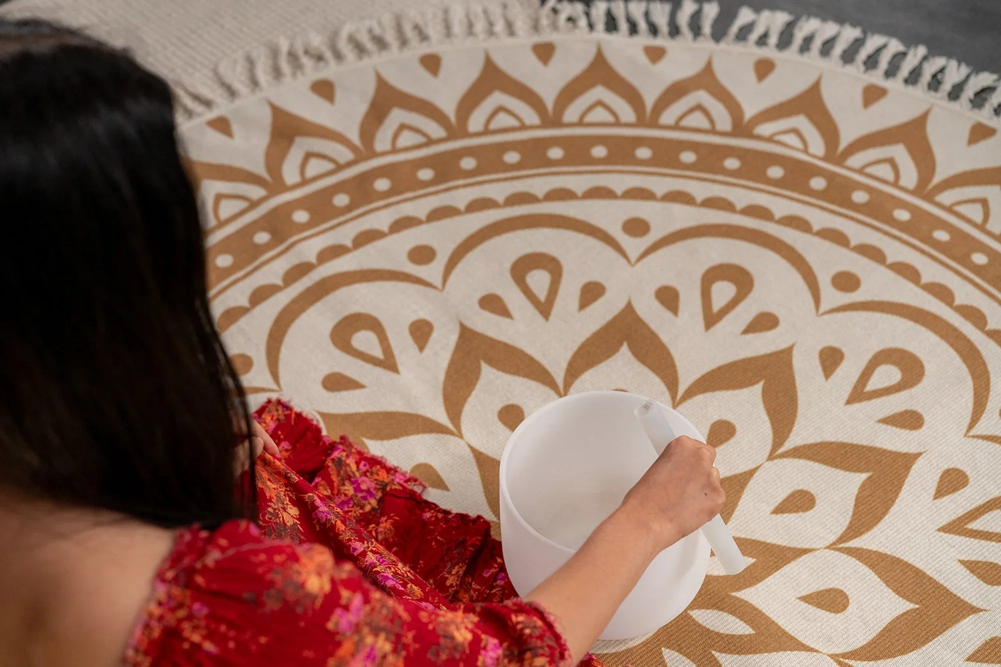 Woman in red dress playing white crystal singing bowl on mandala rug for sound healing