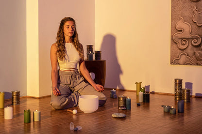 Woman meditating with a crystal singing bowl, candles, and healing crystals on wooden floor