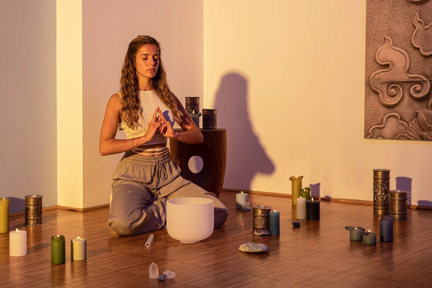 Woman meditating with crystal singing bowl, candles, and crystals in peaceful room