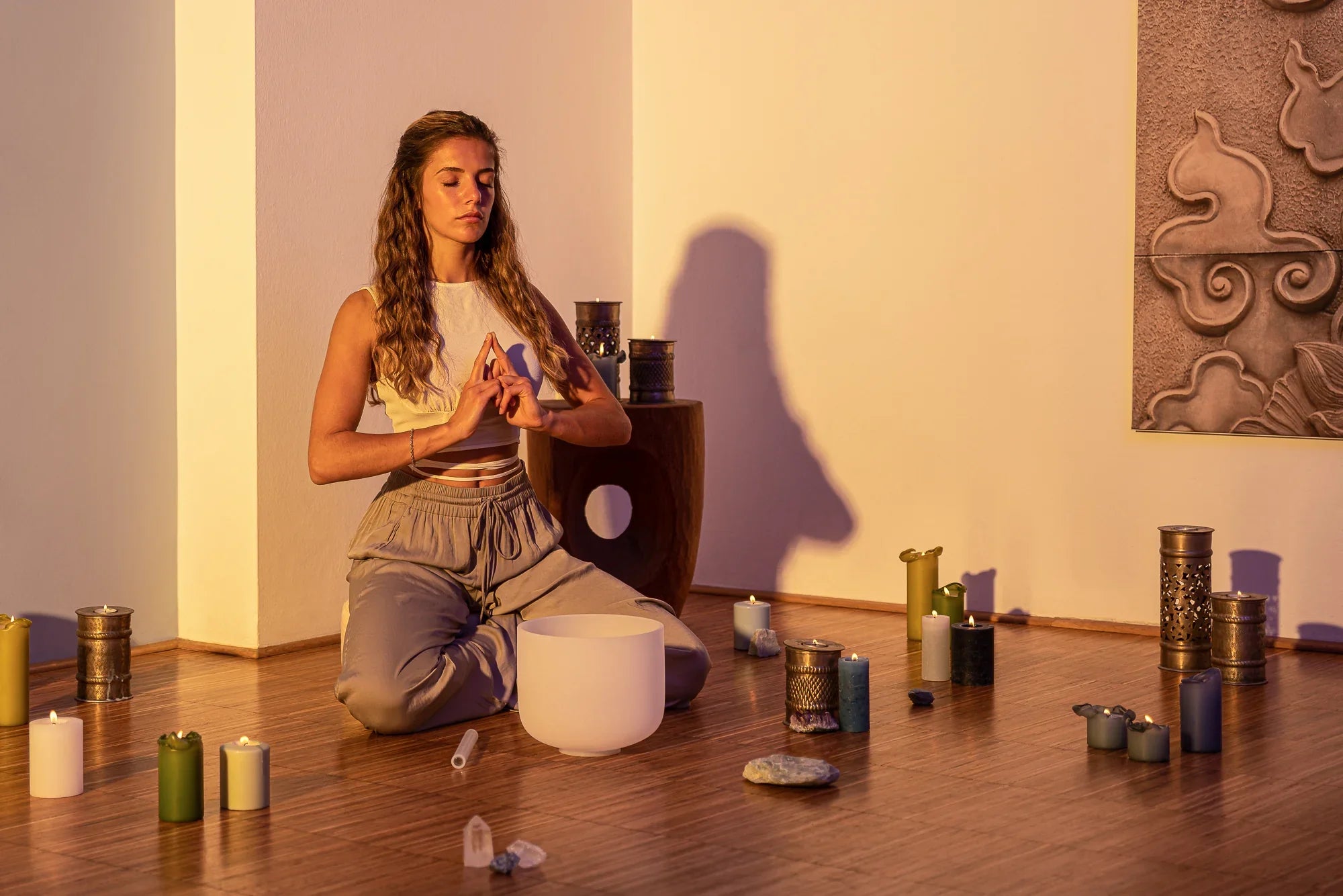 Woman meditating with crystal singing bowl, candles, and crystals in peaceful room