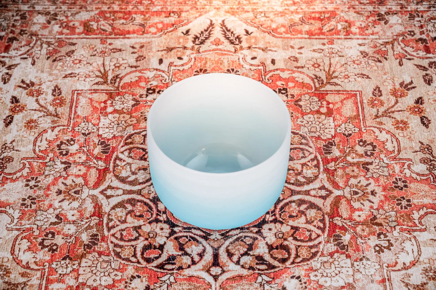 Frosted crystal singing bowl on a patterned floral rug for sound healing