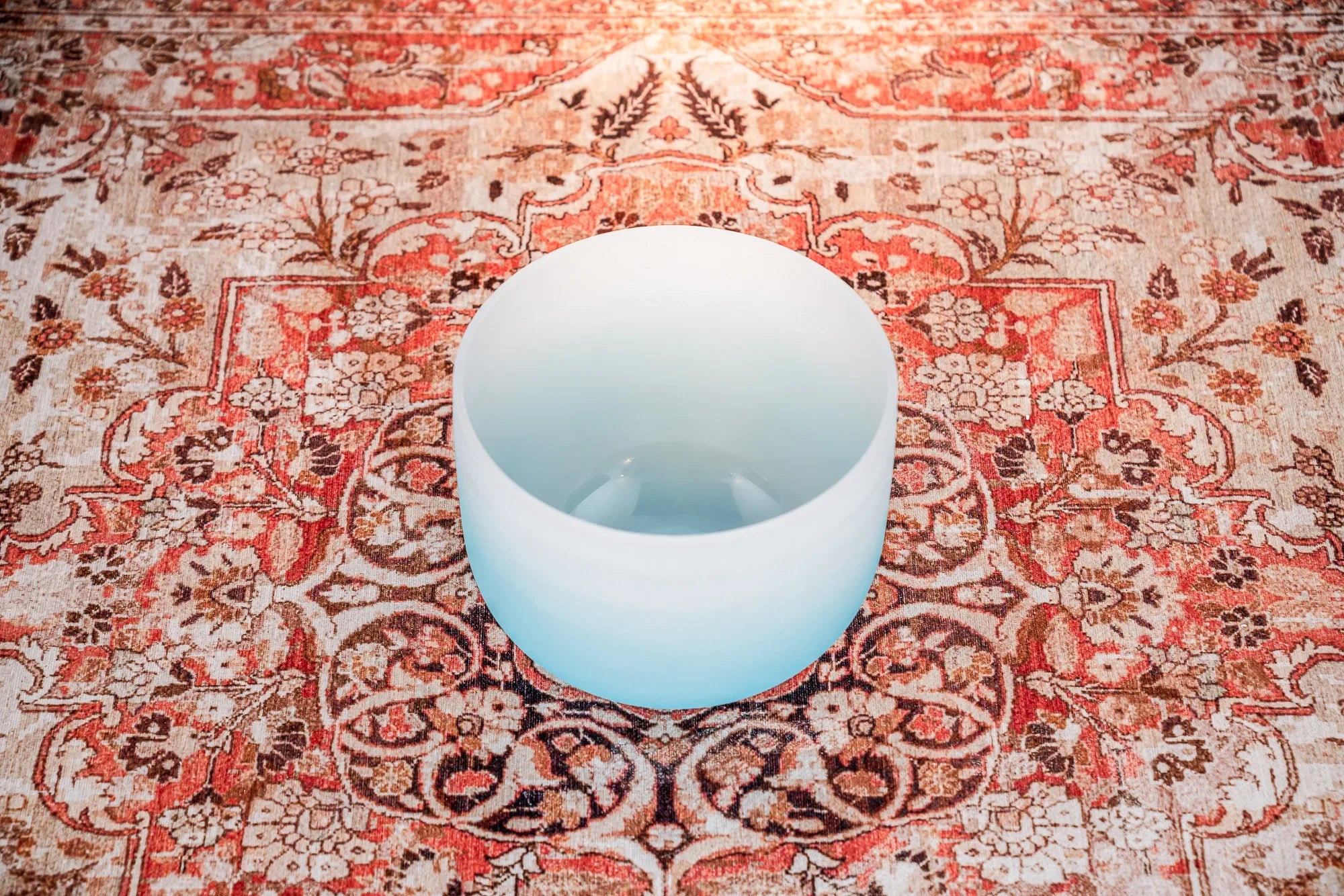 Frosted crystal singing bowl on a patterned floral rug for sound healing