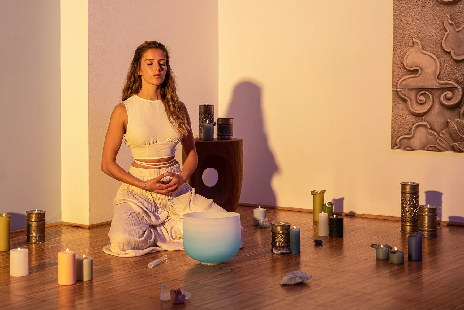 Woman meditating with a frosted crystal singing bowl, candles, and crystals in a peaceful room