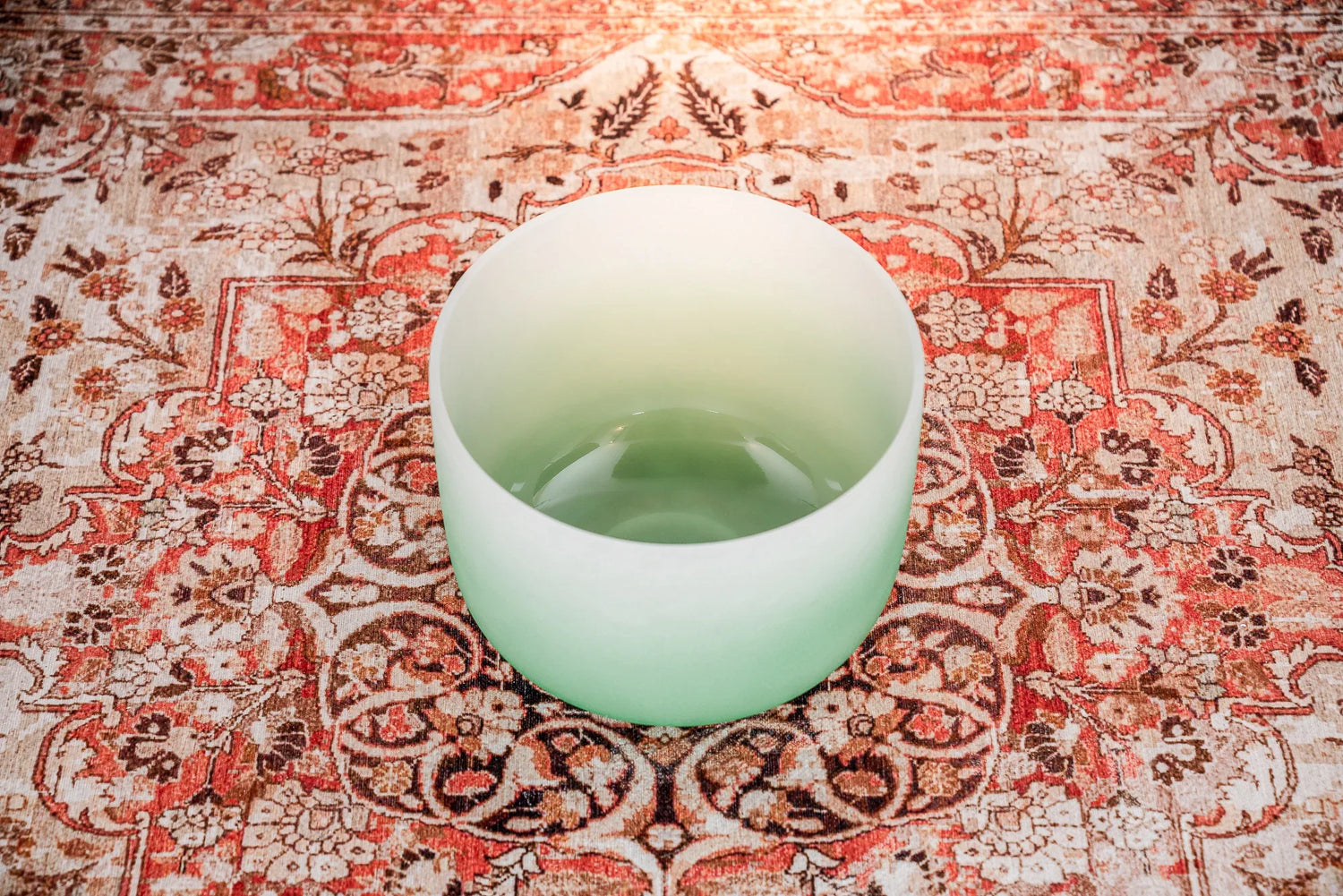 Green frosted crystal singing bowl on patterned rug for sound healing