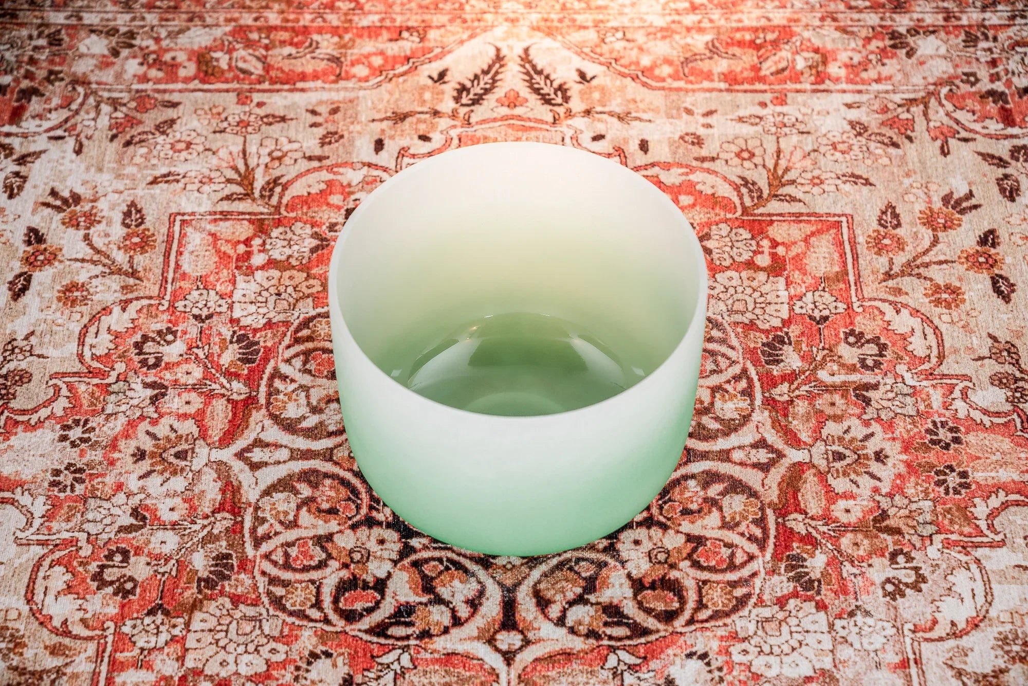 Green frosted crystal singing bowl on patterned rug for sound healing
